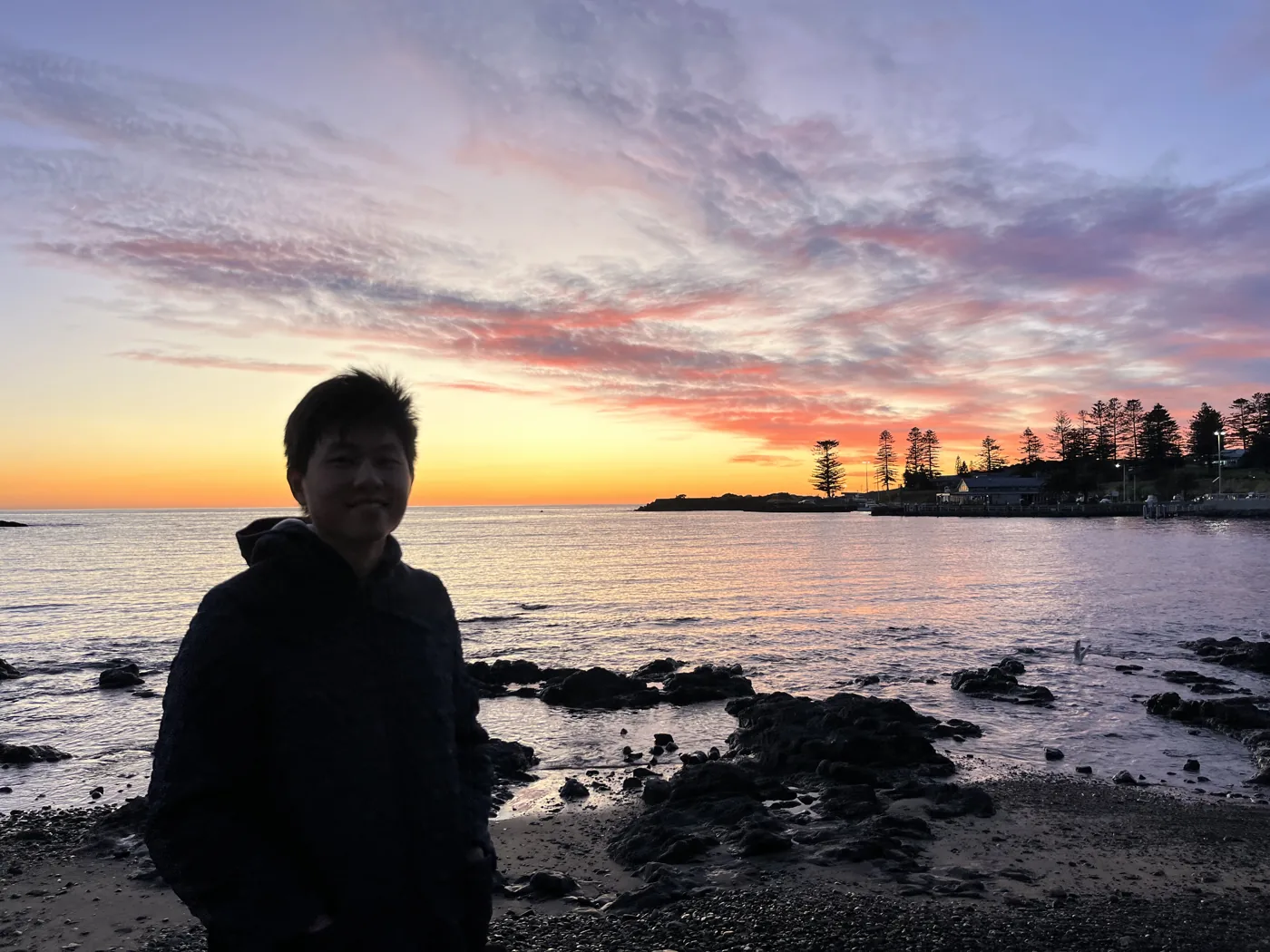 Silhouette standing on a rocky shore at vivid orange and pink sunset