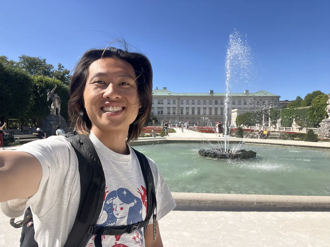 Shin selfie in front of the Mirabell Palace fountain and gardens, water jetting high against a clear blue sky