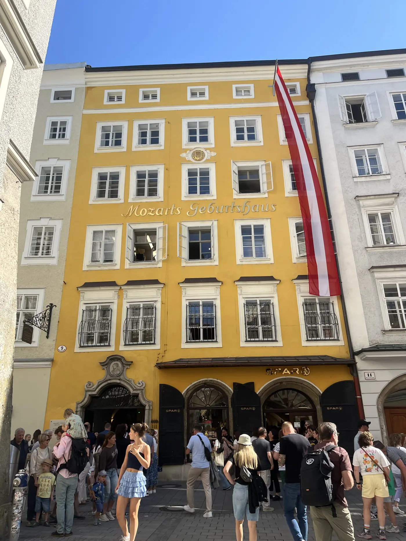 Mozart's birthplace, a yellow building on Getreidegasse marked Mozarts Geburtshaus, with an Austrian flag hanging from the facade and crowds below