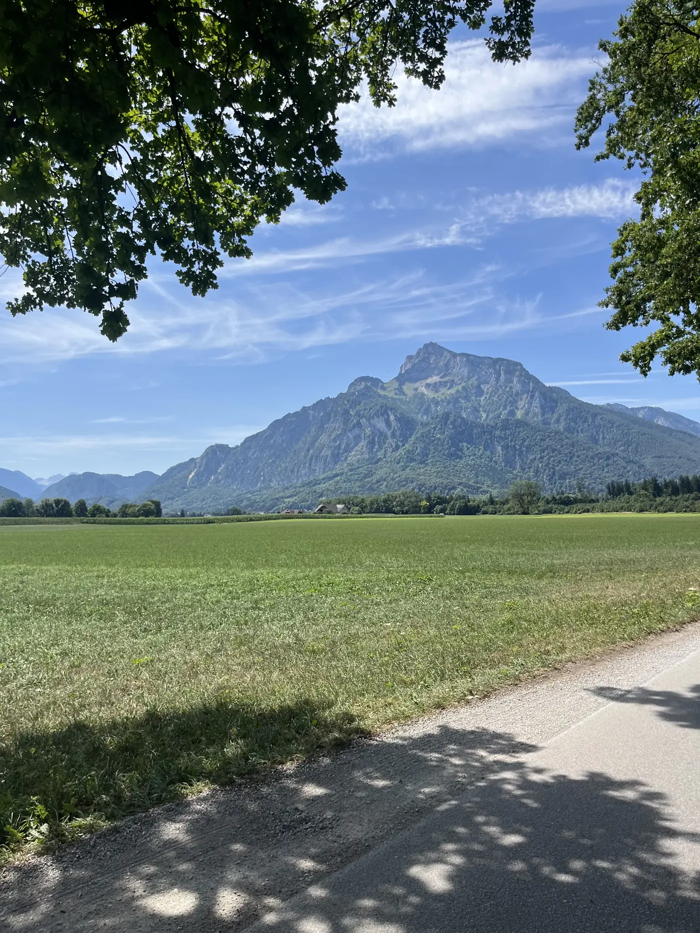 The jagged peak of the Untersberg mountain rising over green farmland on the outskirts of Salzburg under a partly cloudy sky