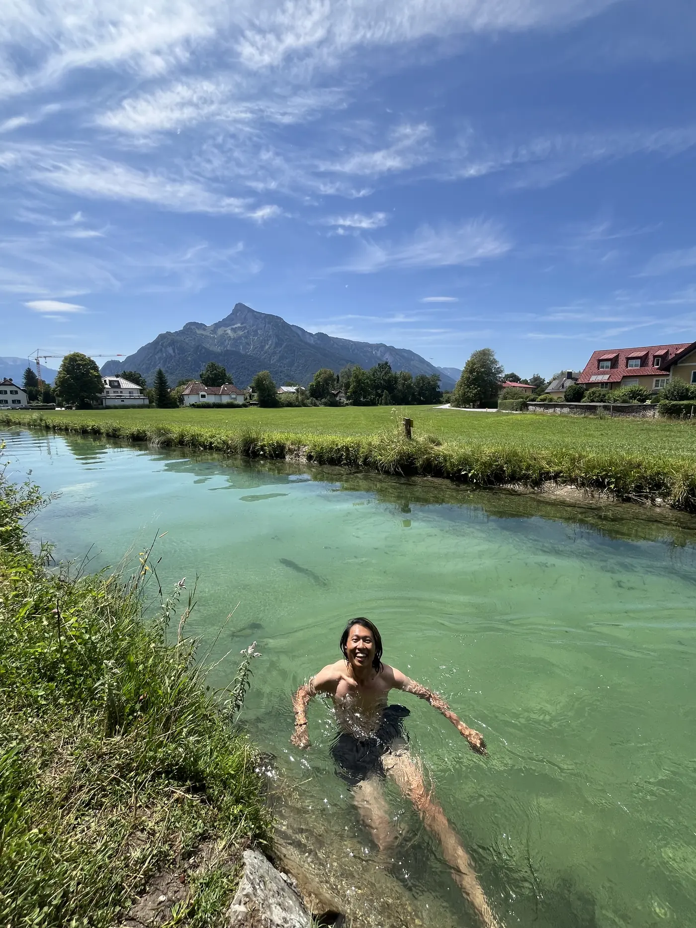 Shin swimming and laughing in a crystal-clear turquoise alpine canal near Salzburg with the Untersberg mountain rising behind him