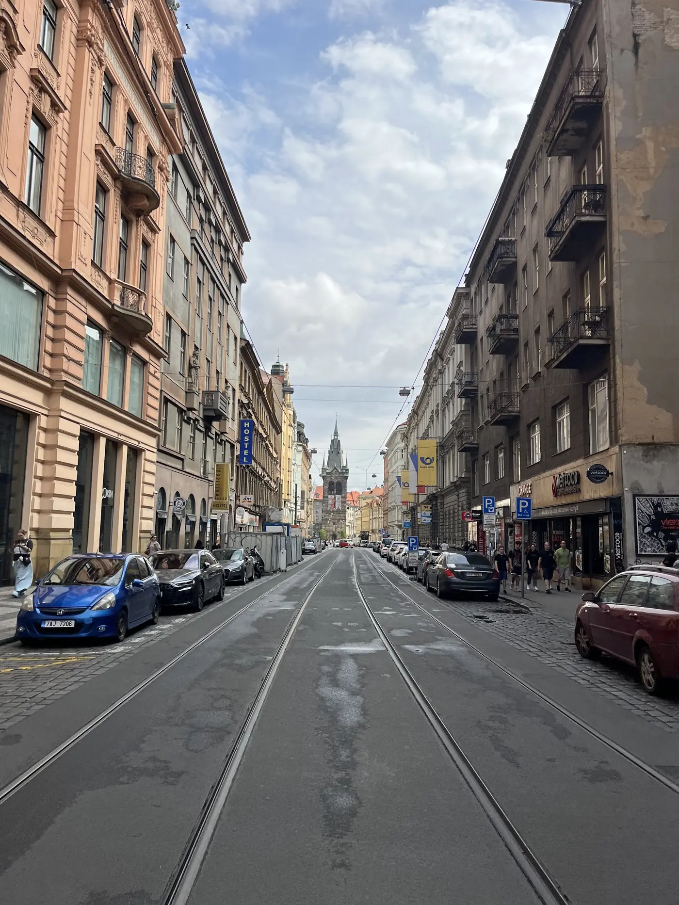 Empty Prague street with tram tracks running down the middle, ornate apartment facades on either side, and the Jindřišská Tower in the distance