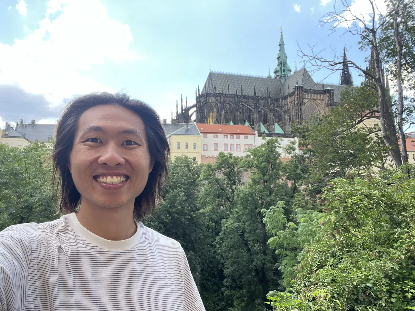Shin selfie with St. Vitus Cathedral's Gothic spires rising above Prague Castle, seen from a green hillside garden
