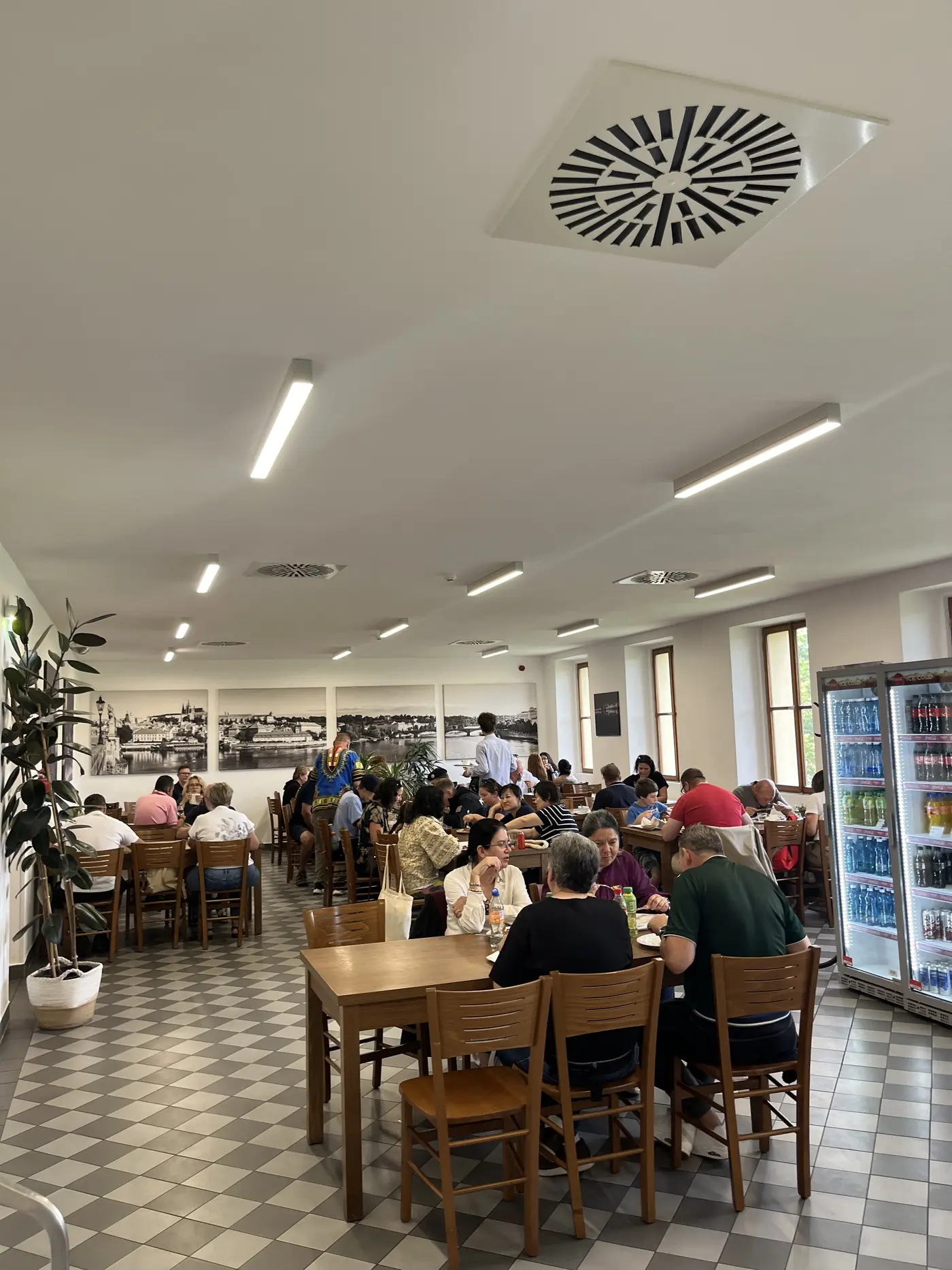 Self-service canteen-style restaurant in Prague with black-and-white photos of the city on the wall and locals eating lunch