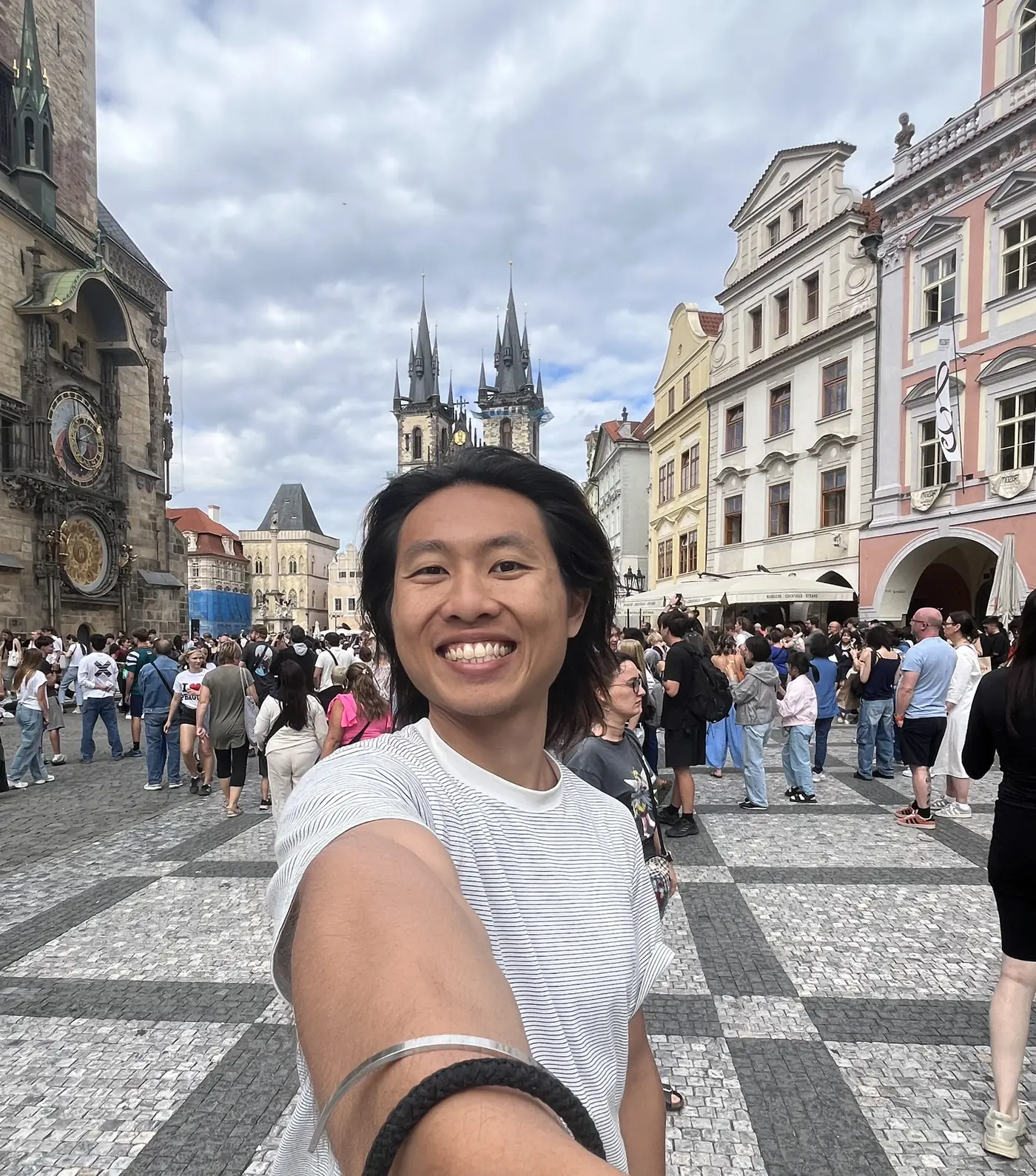 Shin selfie in Prague's Old Town Square with the Astronomical Clock and the twin Gothic spires of the Church of Our Lady before Týn behind him