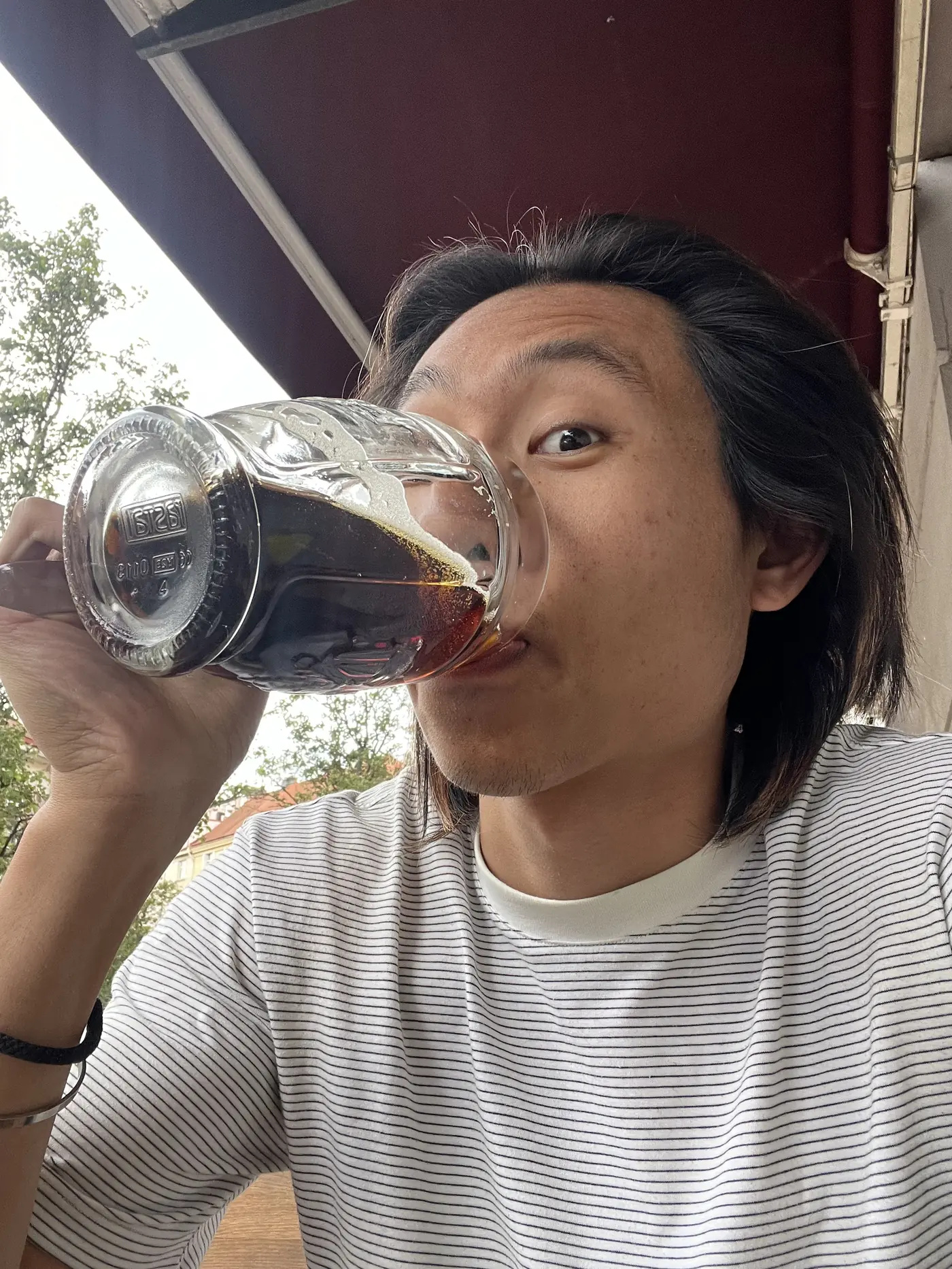 Close-up selfie of Shin drinking a dark Czech beer from a glass mug on an outdoor terrace