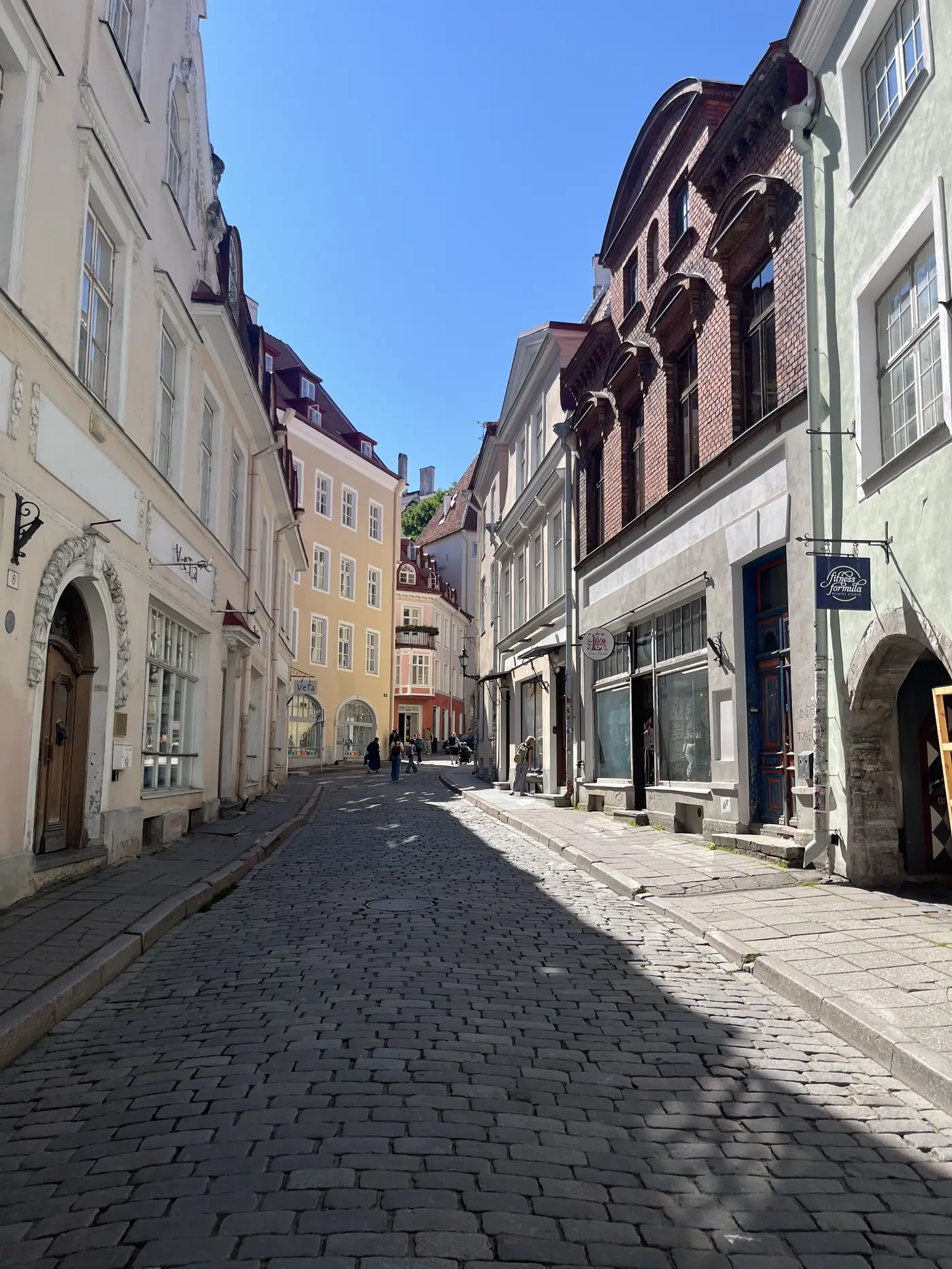 Empty cobblestone street in Tallinn's Old Town lined with pastel medieval buildings, shops and a distant church tower