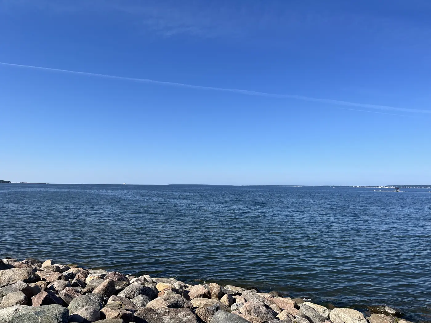 Calm Baltic Sea coastline near Tallinn with a rocky shoreline in the foreground and a distant hazy horizon under clear blue sky