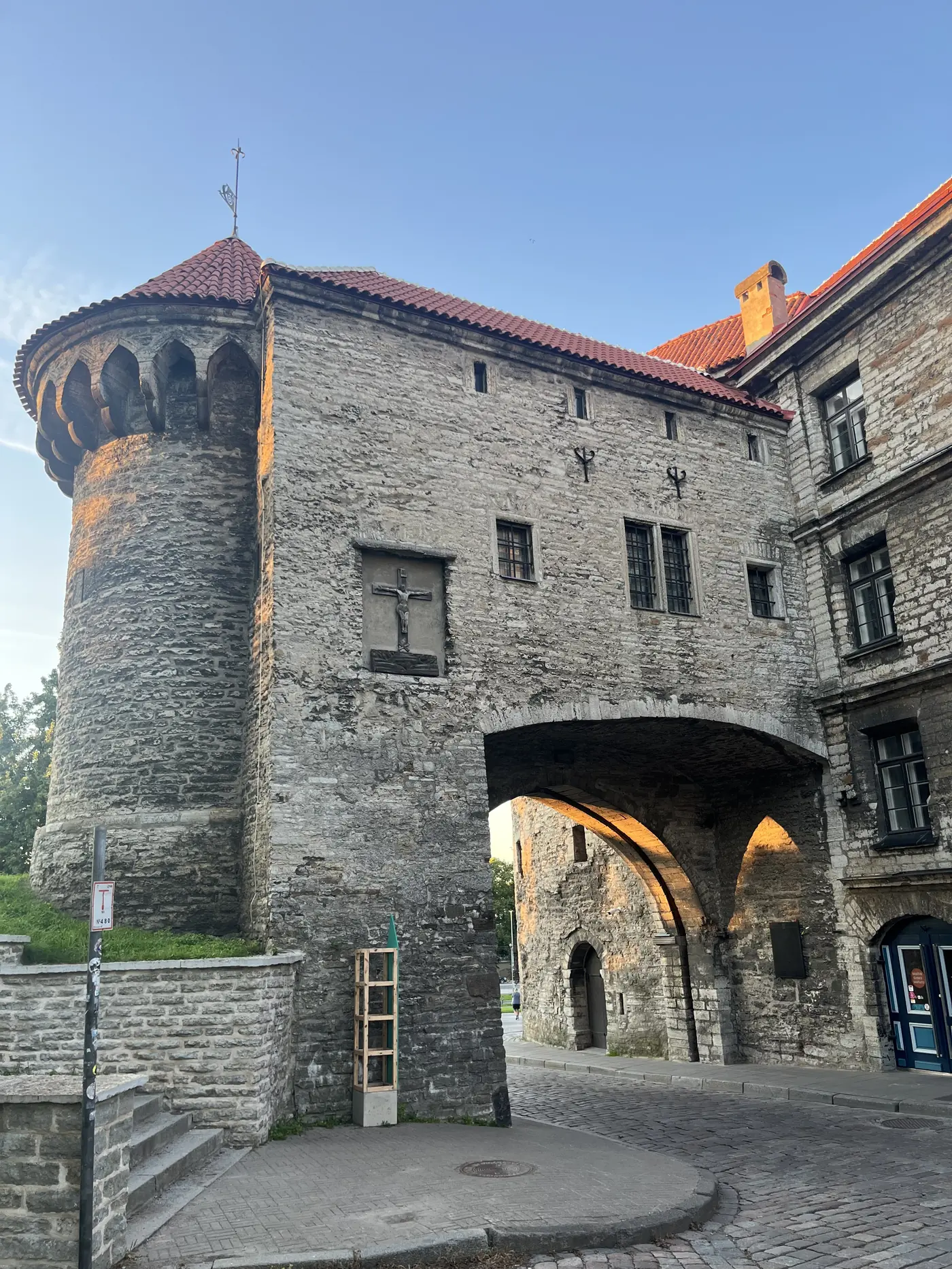 Medieval stone gate tower in Tallinn's Old Town wall with a conical red-tiled roof, crucifix relief, and an archway leading into the city