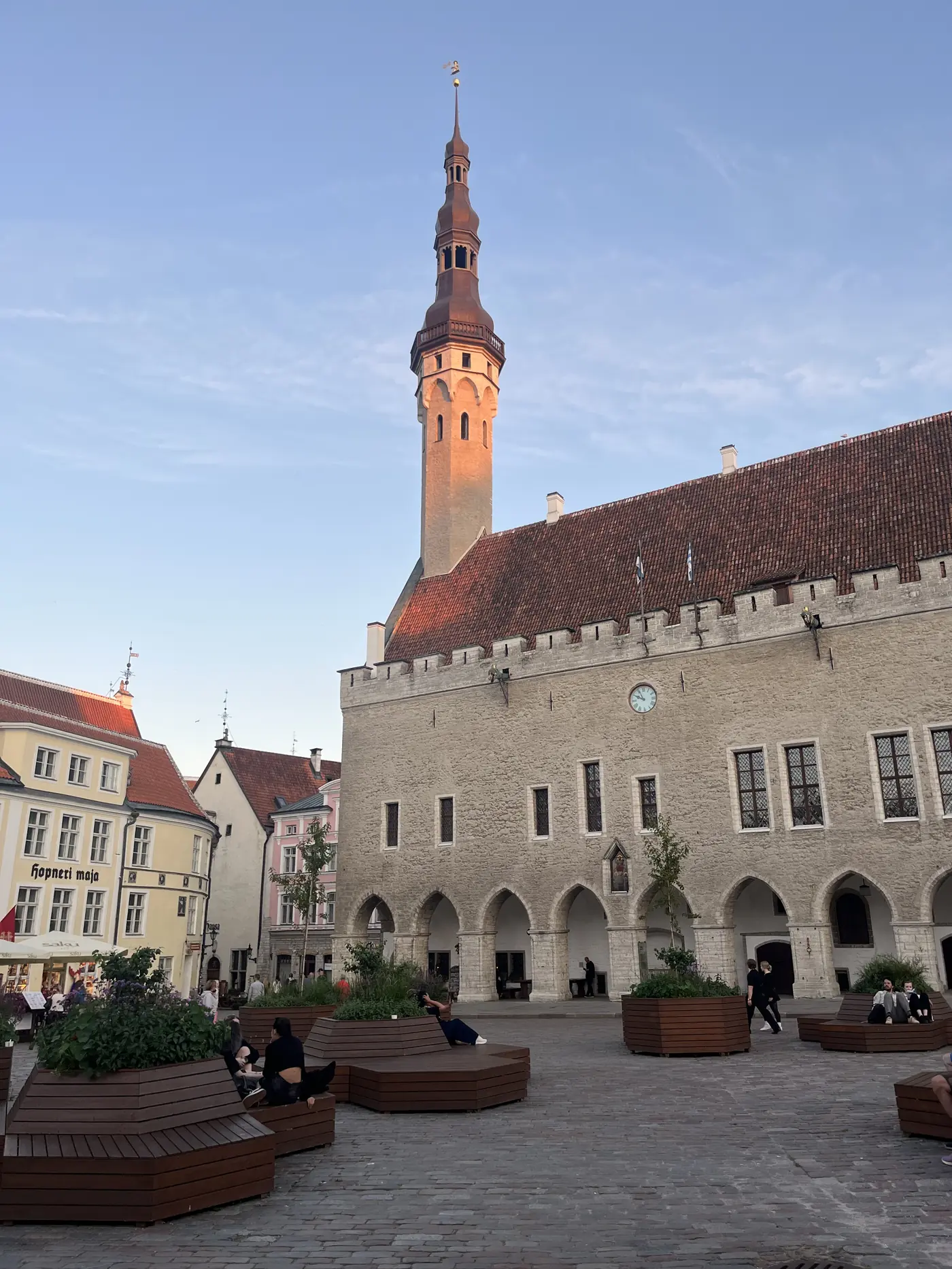 Tallinn Town Hall Square at dusk with the Gothic Town Hall tower spire glowing in the last light and cafe terraces below