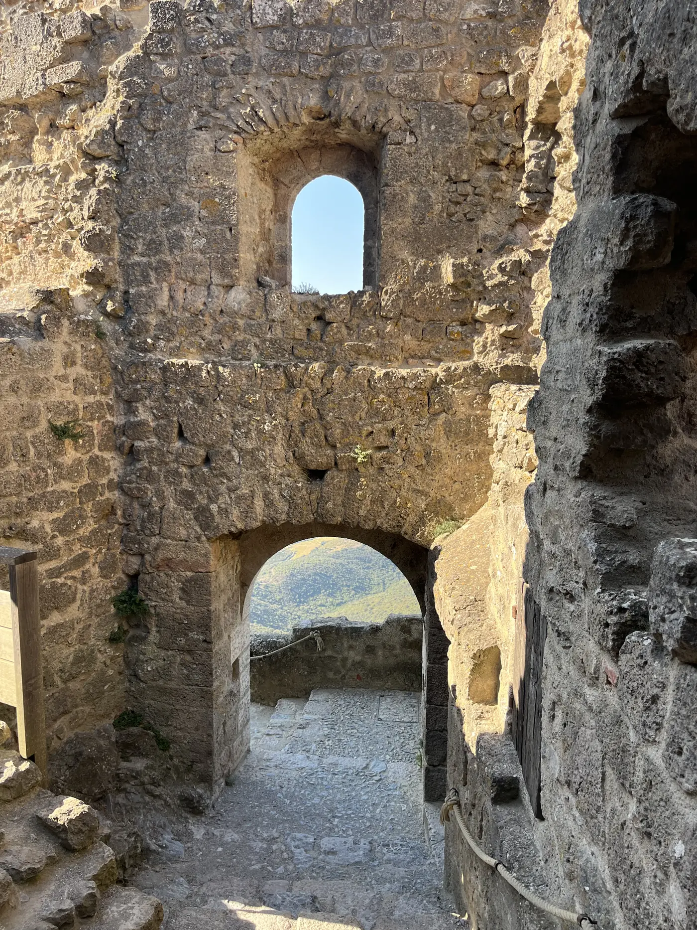 Ruined stone archway and tower inside a medieval Cathar castle in the Corbières hills, mountain view through the gap