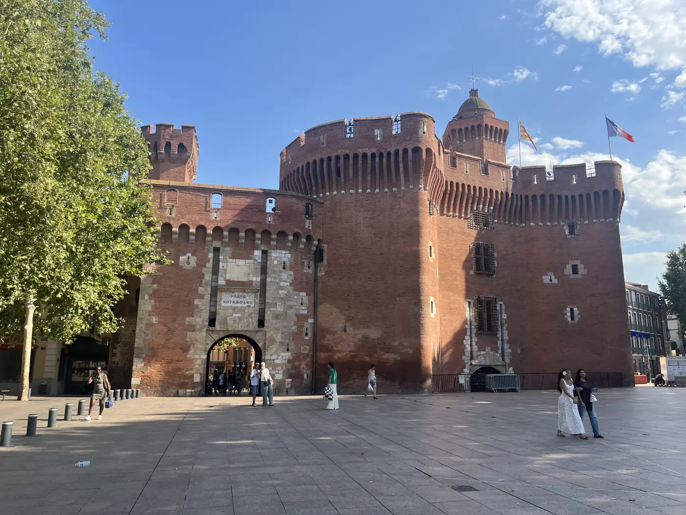 Le Castillet, Perpignan's iconic red-brick fortified gate tower with crenellations, standing in a sunny plaza