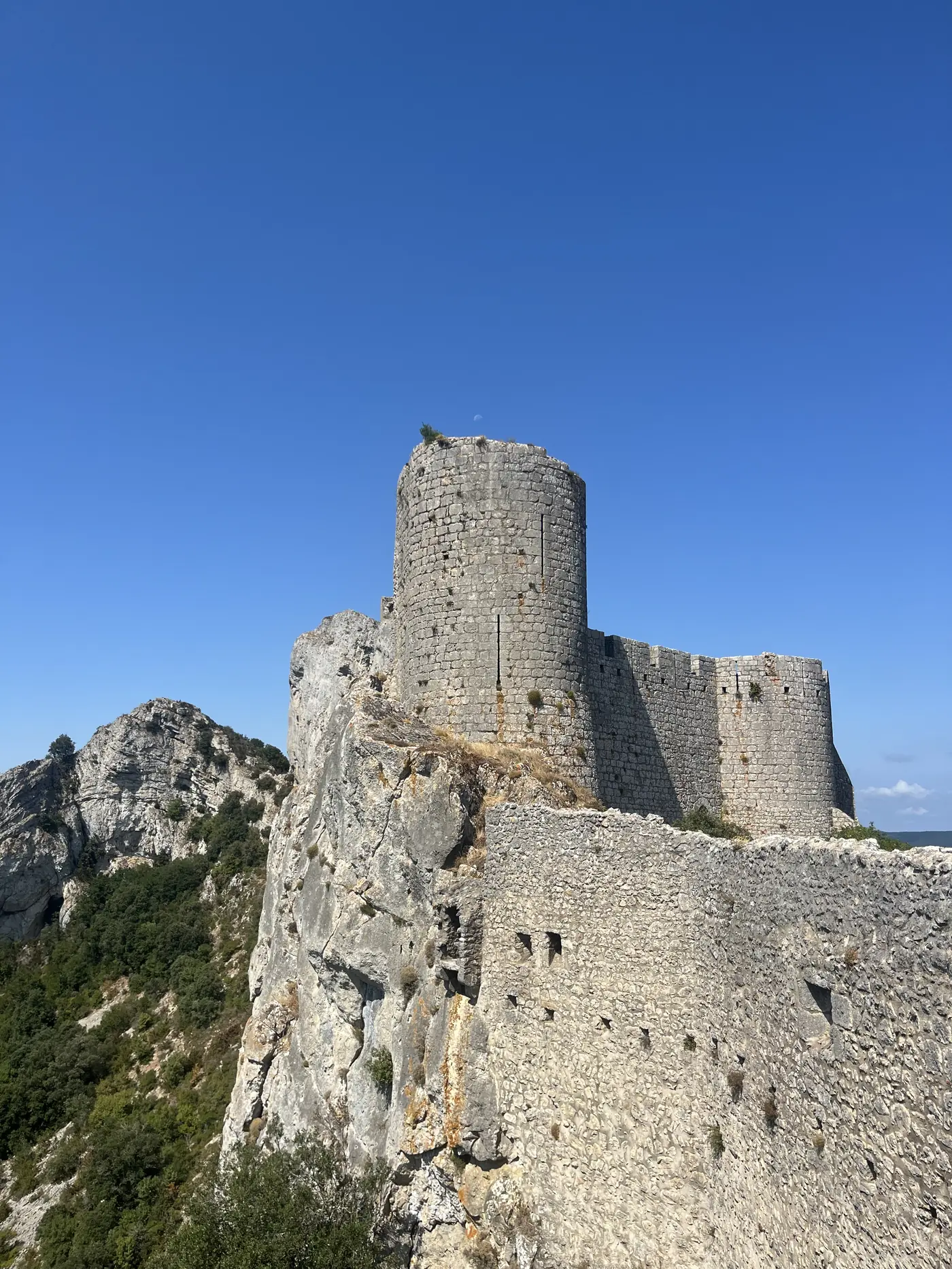 The distinctive round keep of Château de Peyrepertuse perched on a jagged limestone ridge against a clear blue sky