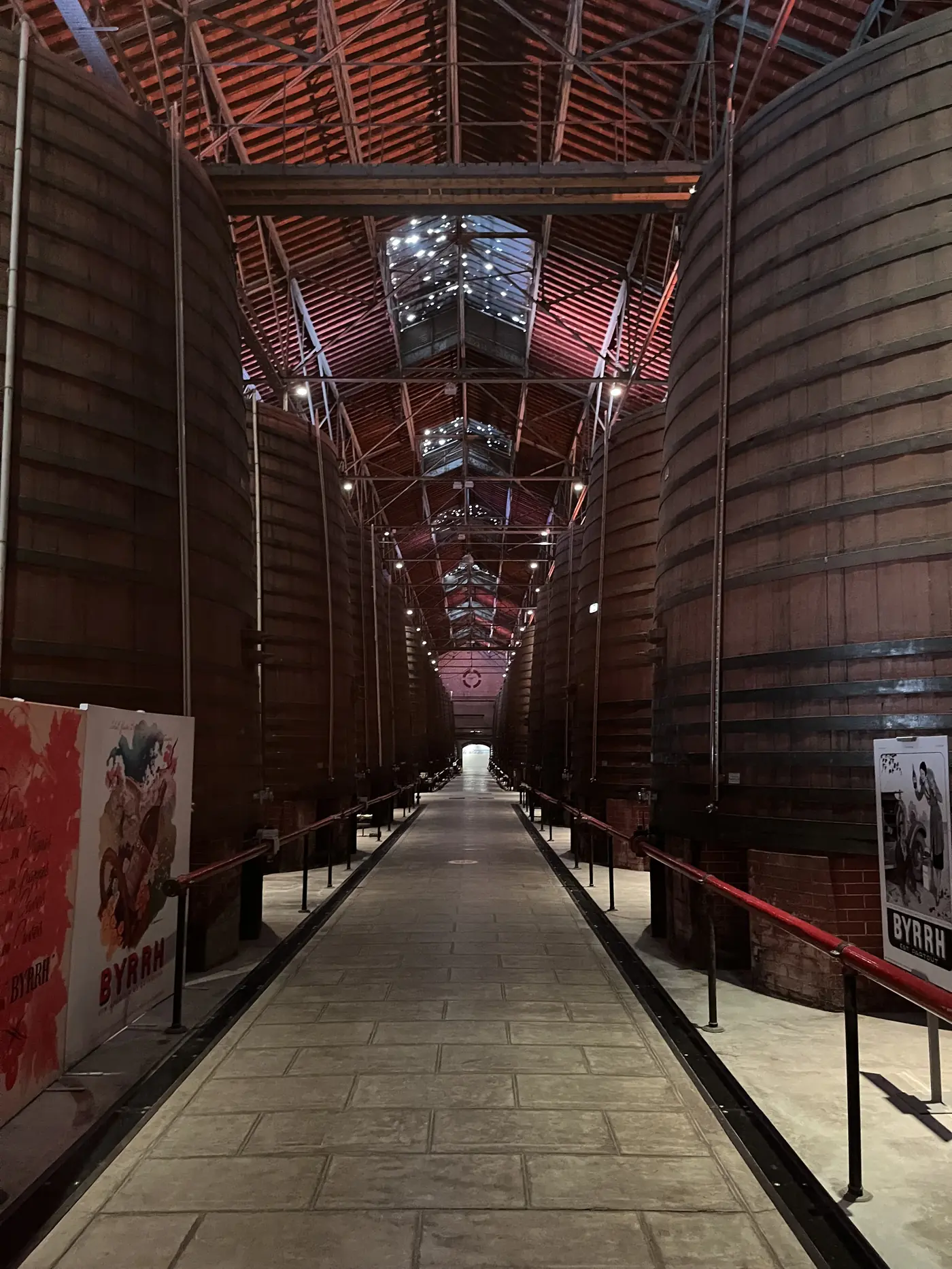 Rows of giant oak vats inside the Byrrh cellars in Thuir, France, lit by skylights running along a vaulted wooden roof