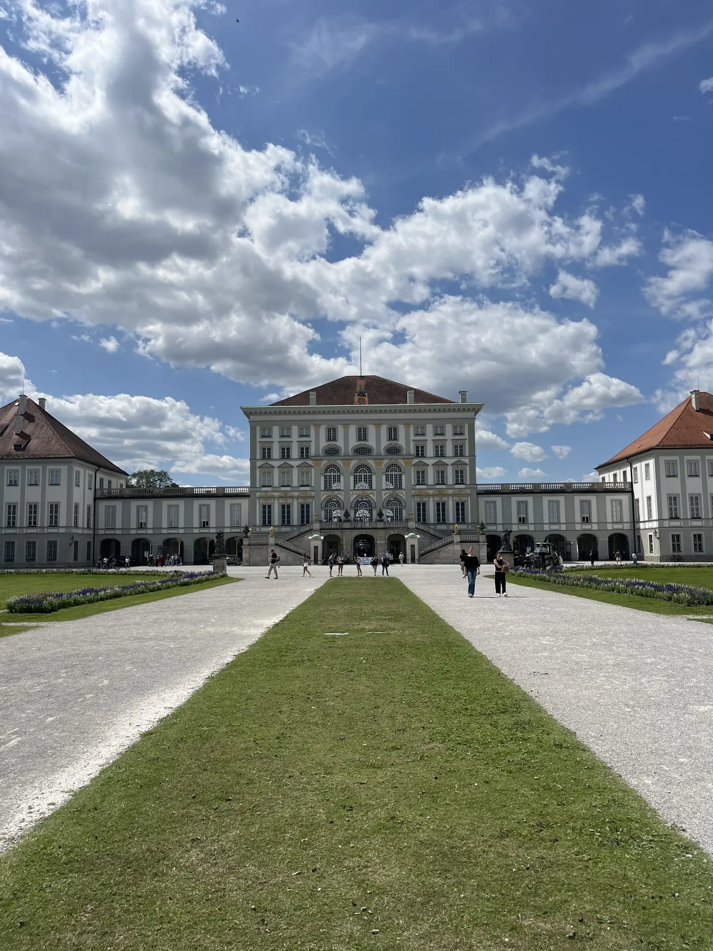 Nymphenburg Palace's baroque facade viewed from across its formal gardens, flanked by symmetrical pavilions under a blue sky