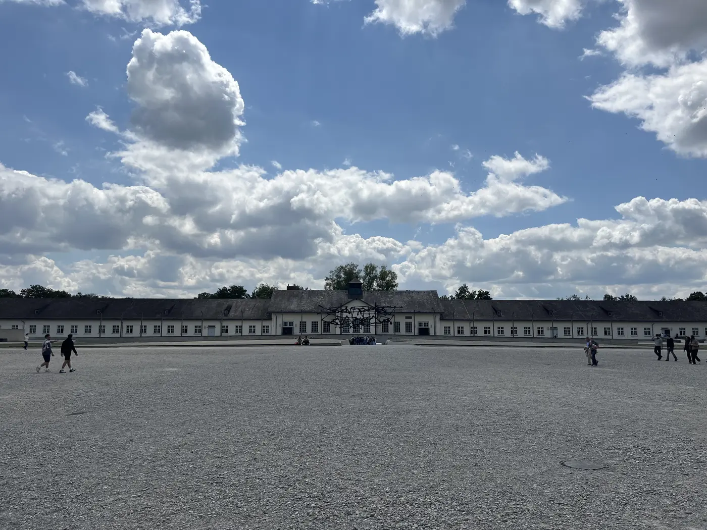 The wide roll-call square at the Dachau Memorial Site, with the former maintenance building and the International Memorial sculpture in the distance