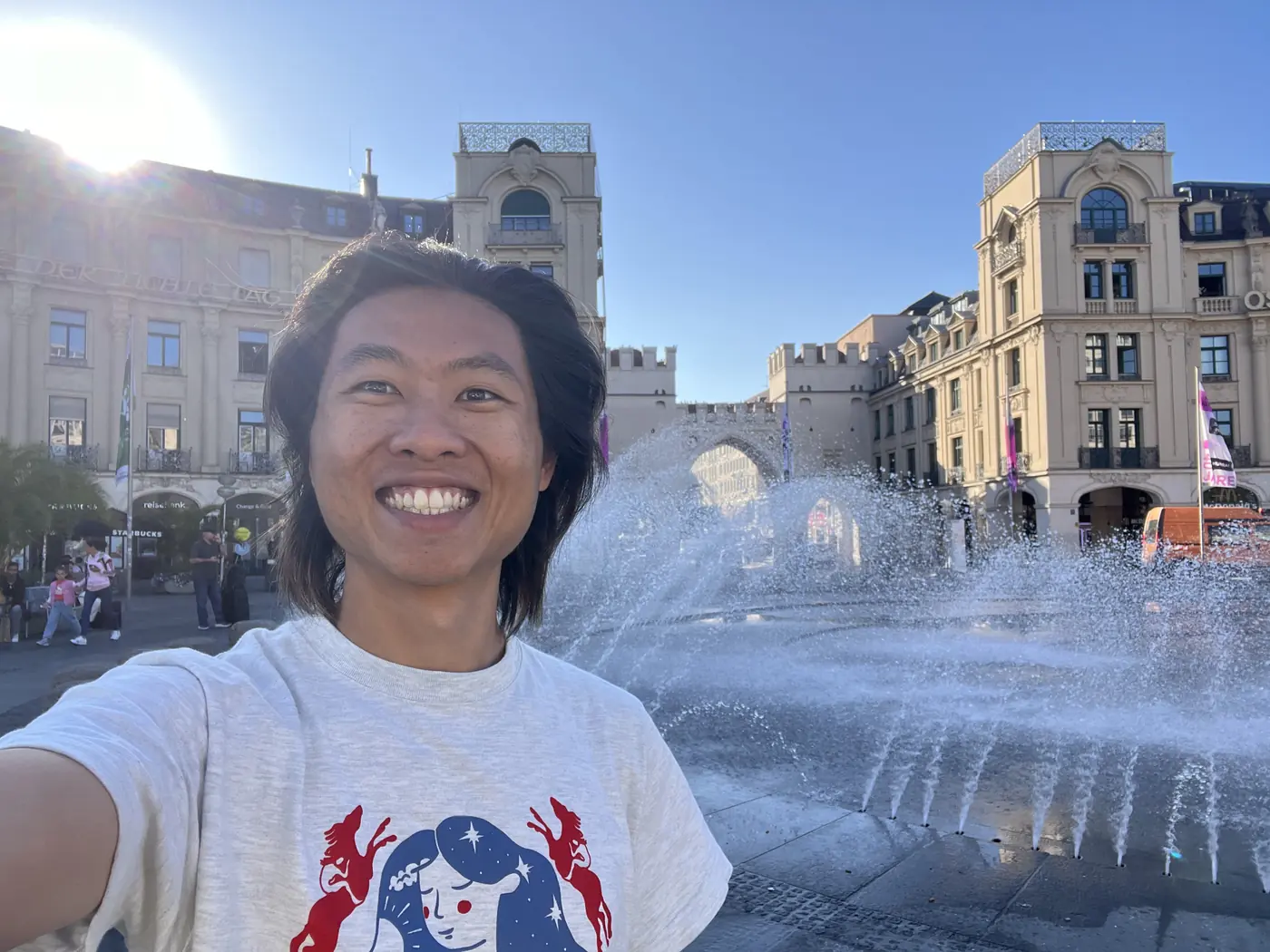 Shin selfie in front of the Karlstor gate and Stachus fountain in Munich, sunlight flaring over the historic buildings
