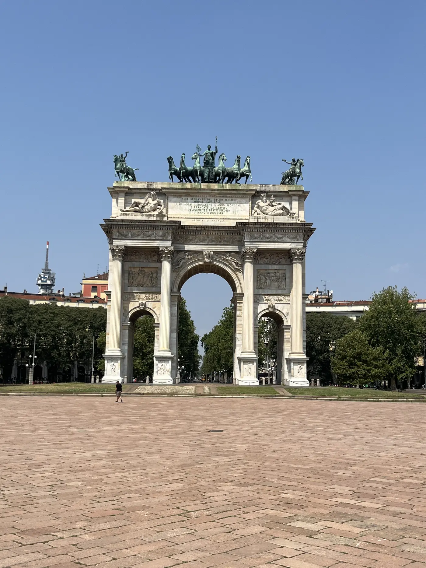 Wide view of the Arco della Pace triumphal arch in Milan, bronze chariot statues on top, empty plaza in the morning light