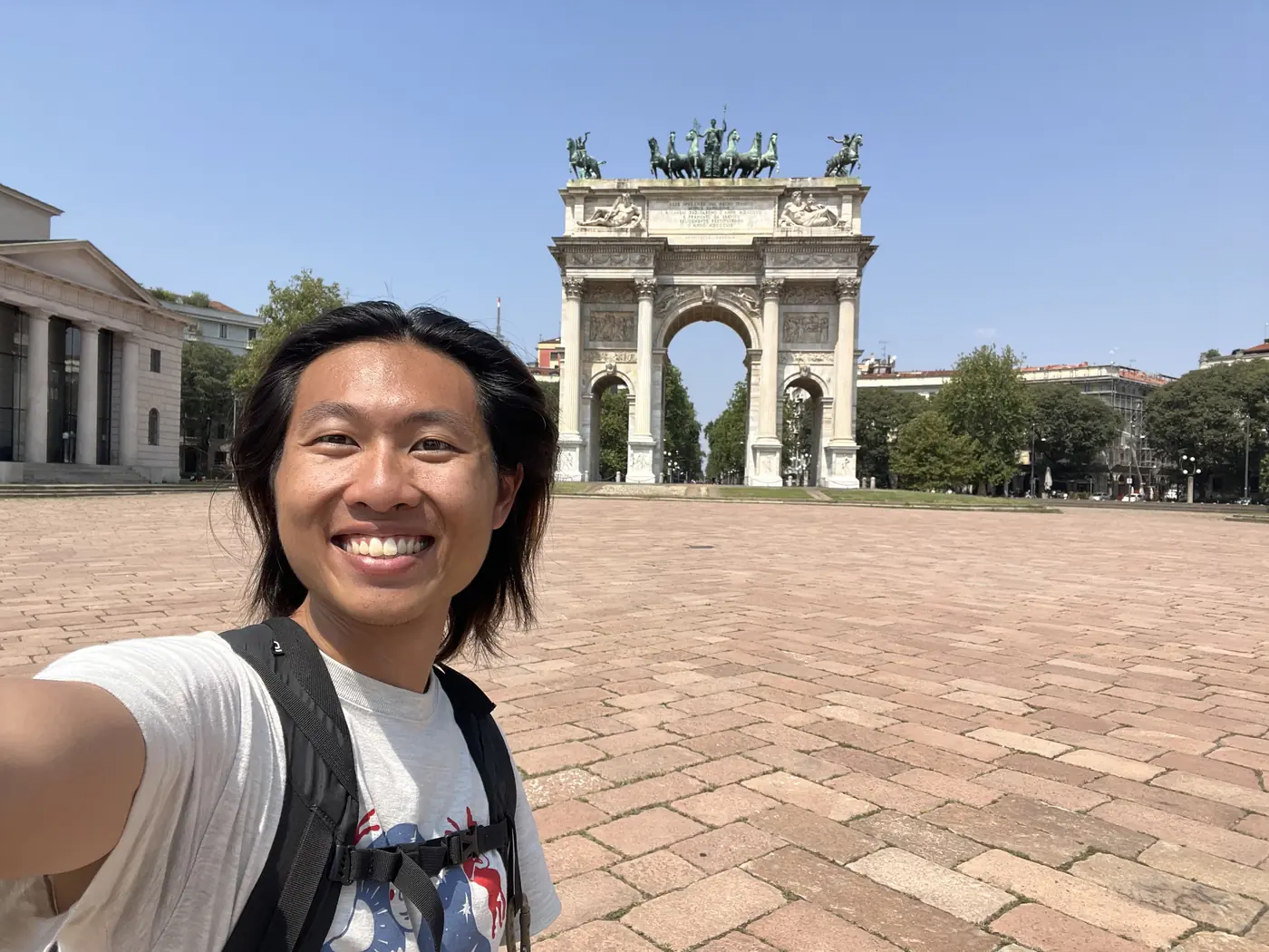 Shin selfie in front of the Arco della Pace, a neoclassical triumphal arch topped with a bronze chariot sculpture, Milan