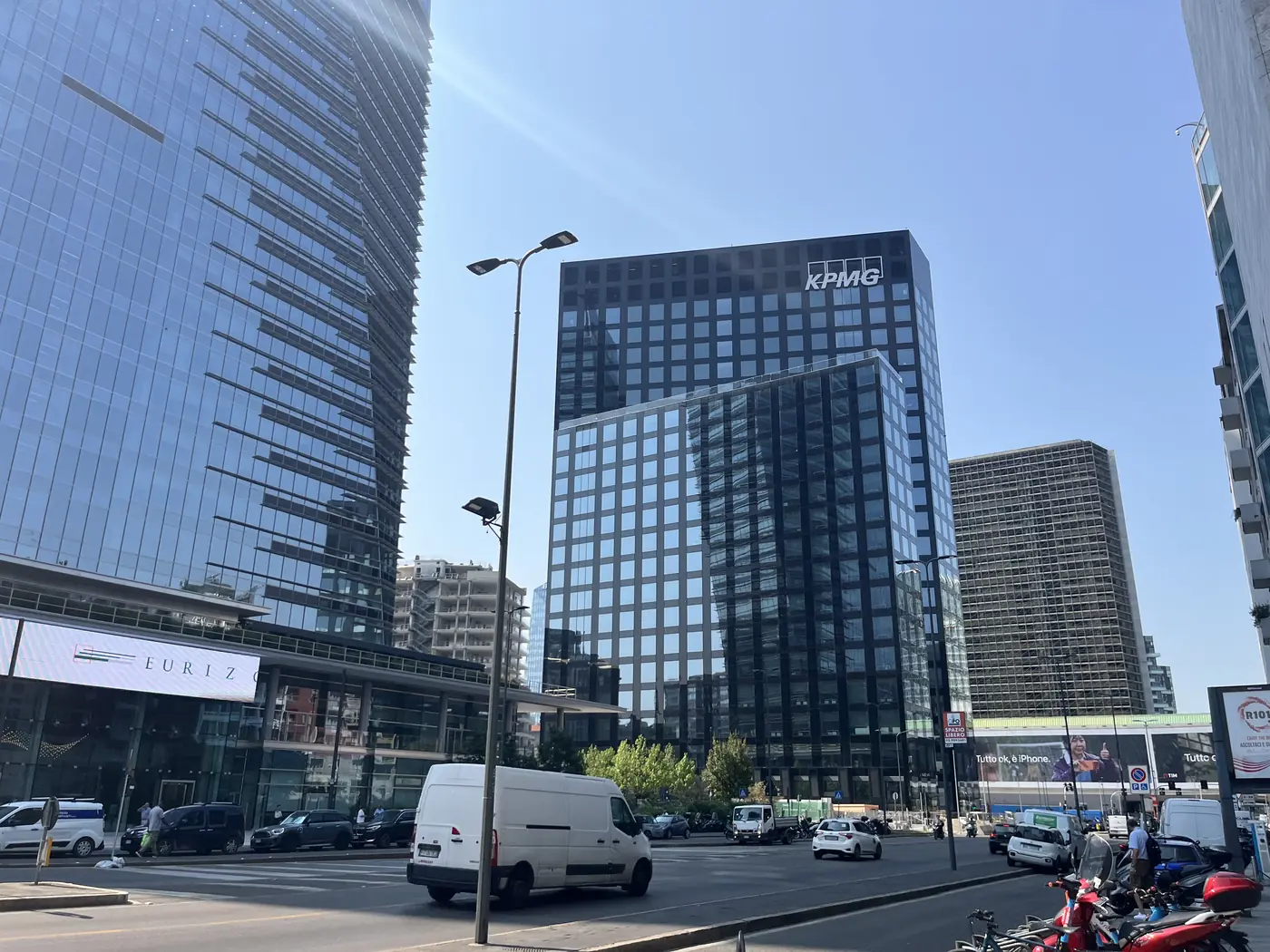 Modern glass skyscrapers in Milan's Porta Nuova business district, including a KPMG office tower, with cars on the street below