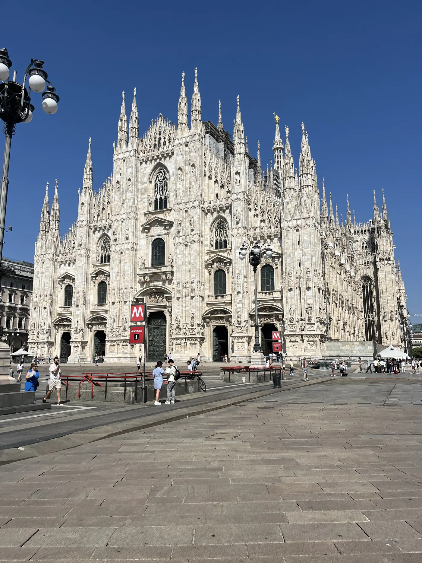 Milan Cathedral's full white marble Gothic facade with hundreds of spires, seen across a wide Piazza del Duomo
