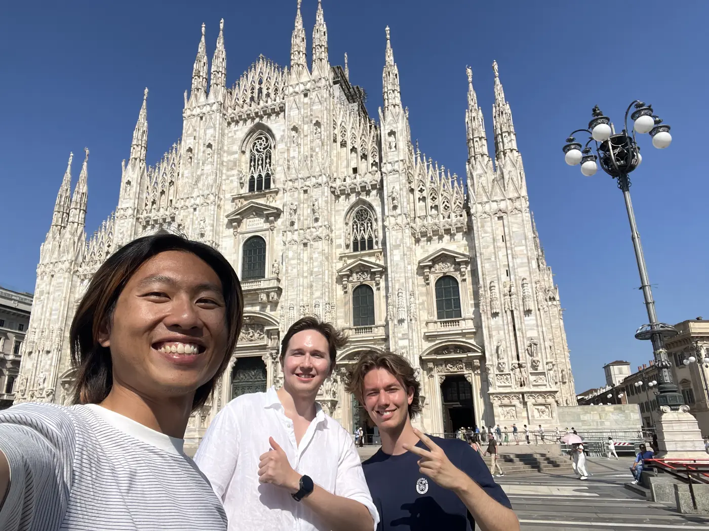 Shin and two friends smiling in front of Milan Cathedral's white Gothic facade in Piazza del Duomo