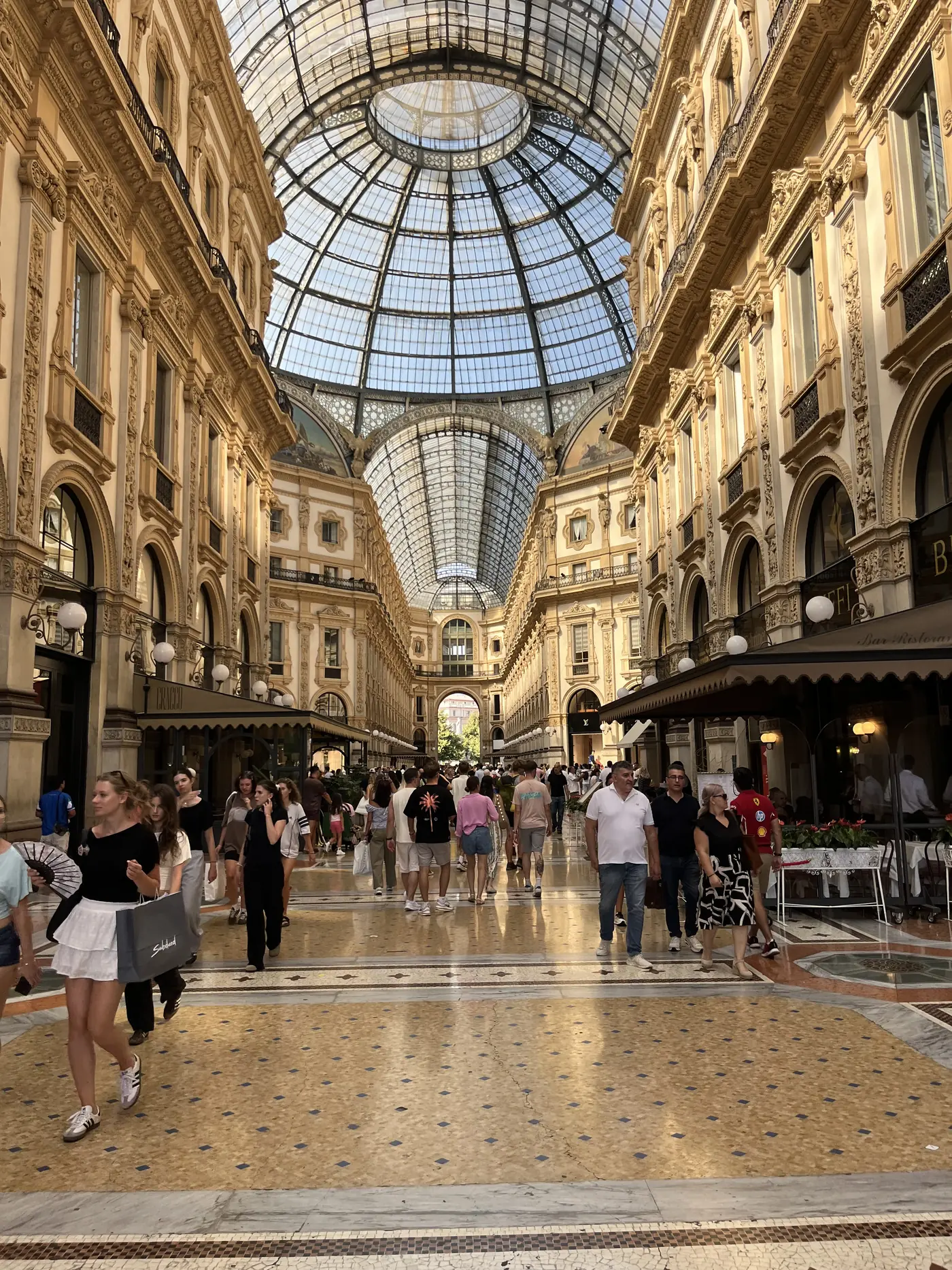 The Galleria Vittorio Emanuele II in Milan, an ornate glass-and-iron domed shopping arcade with mosaic floors and crowds strolling underneath