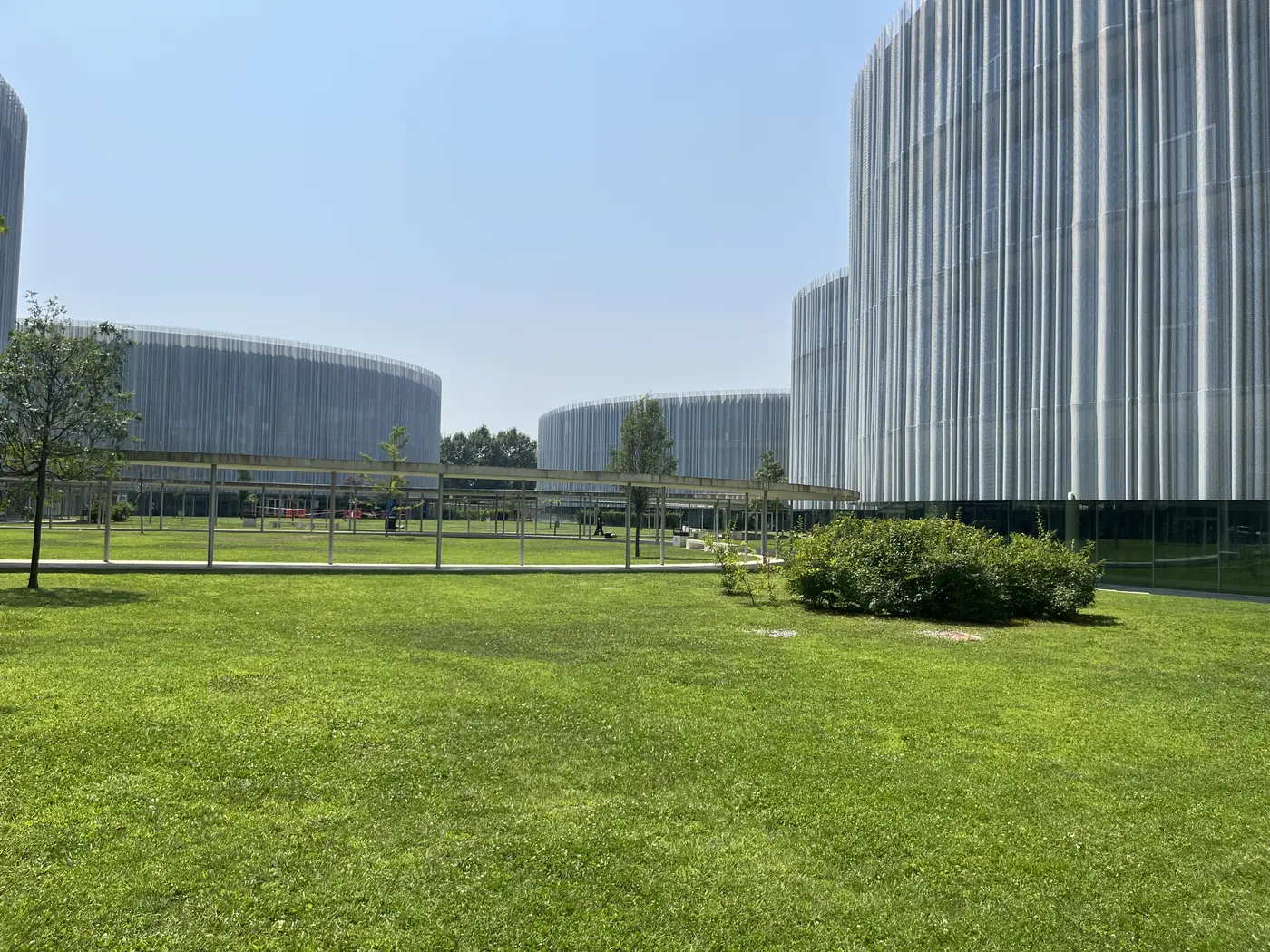 Modern cylindrical silver-clad university buildings surrounding a green lawn on Bocconi University's campus in Milan