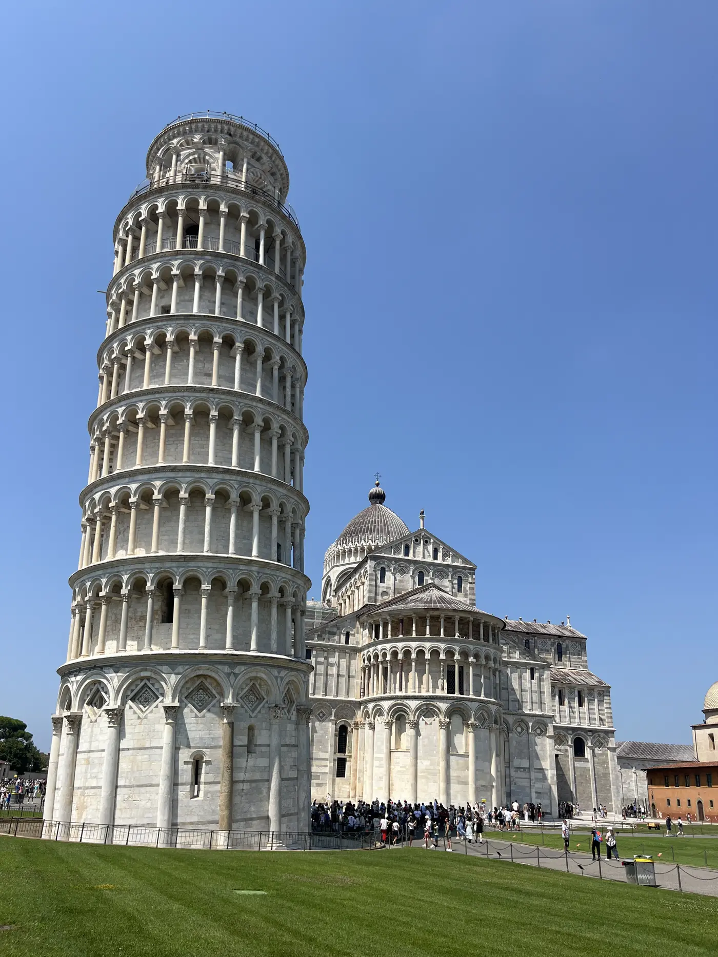 The Leaning Tower of Pisa and Pisa Cathedral seen from the lawn of the Piazza dei Miracoli under a clear blue sky