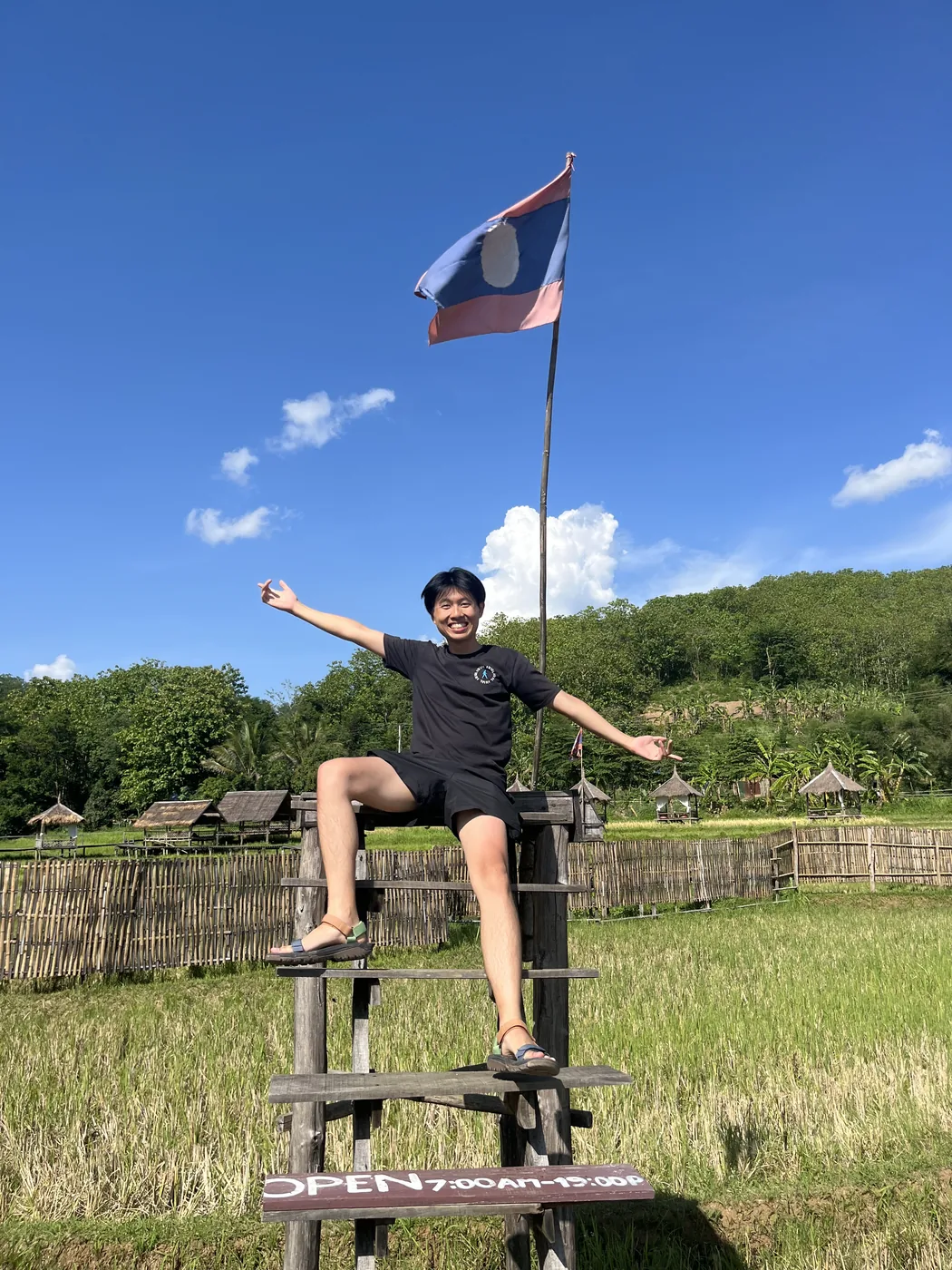 Posing with Lao flag at hilltribe village watchtower, Laos