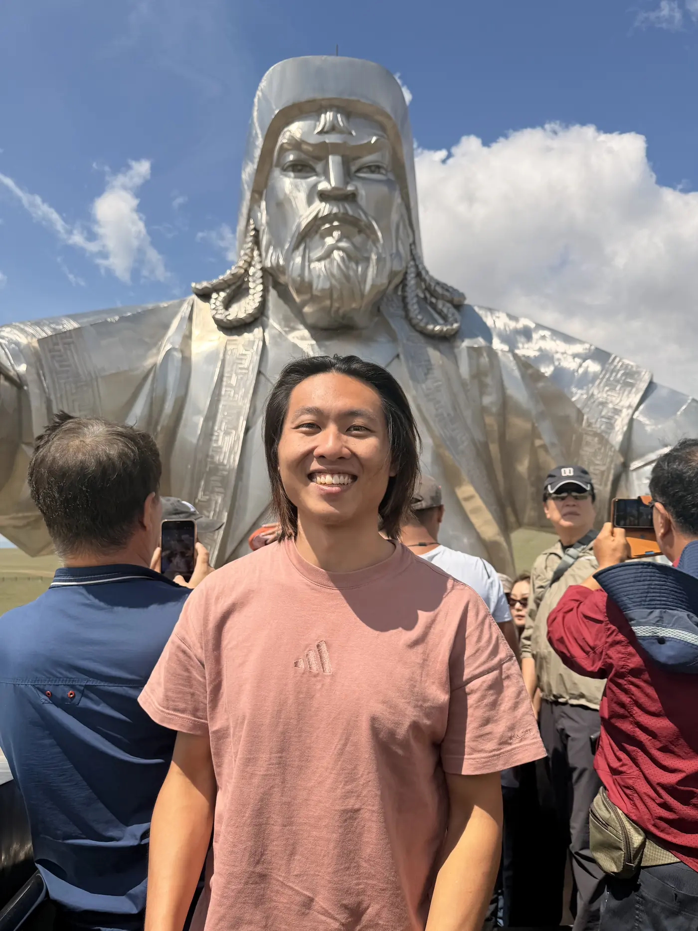 Shin posing in front of the giant Genghis Khan face sculpture at Tsonjin Boldog statue complex, Mongolia, with tourists around him