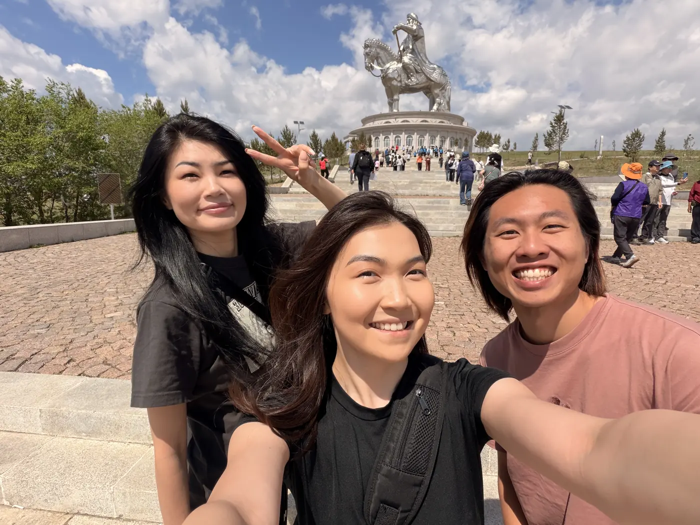 Group selfie of three friends in front of the Genghis Khan equestrian statue complex near Ulaanbaatar, Mongolia, sunny day
