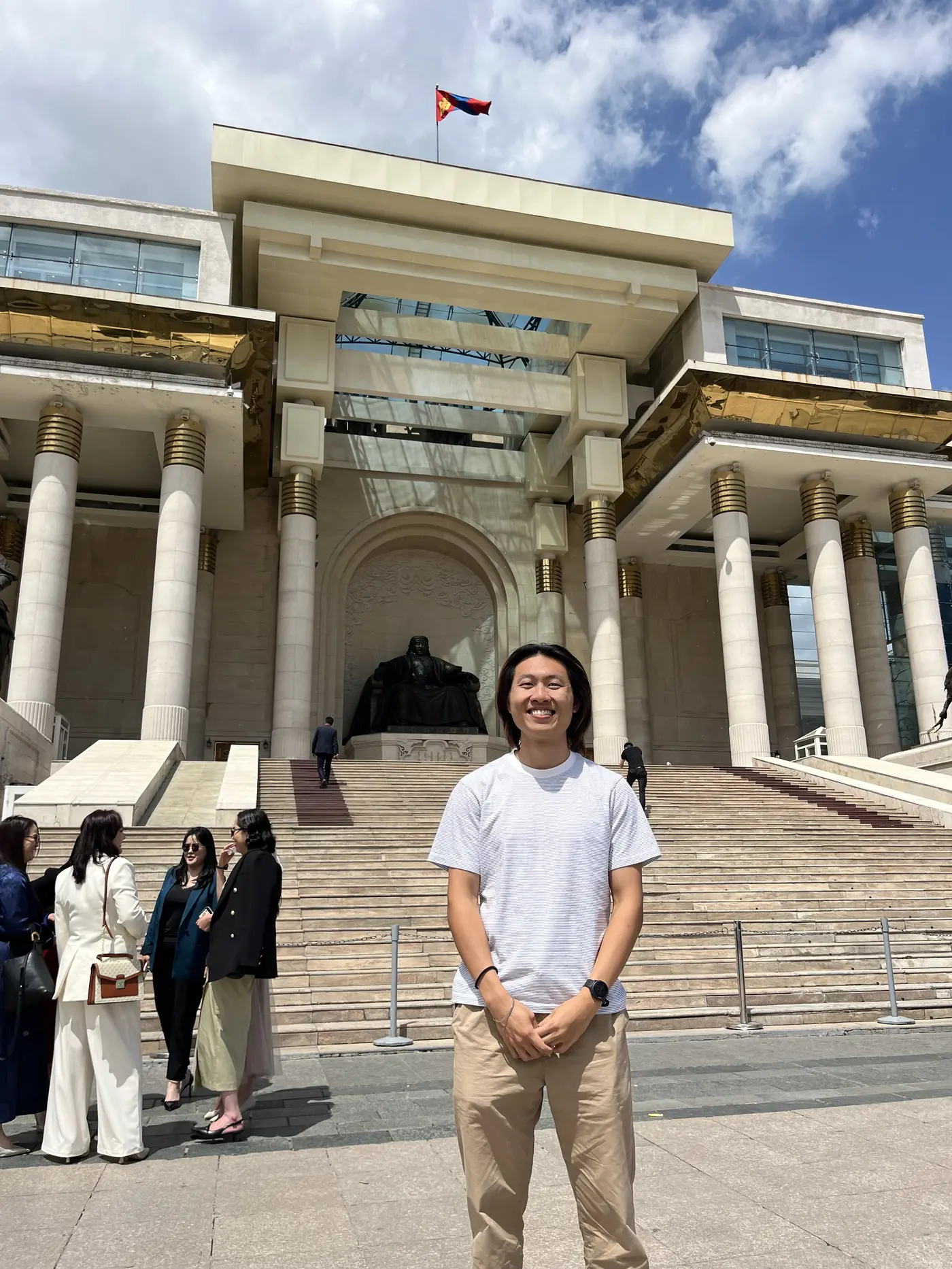 Solo traveller Shin standing in front of the Government Palace on Sukhbaatar Square, Ulaanbaatar, with Mongolian flag flying above