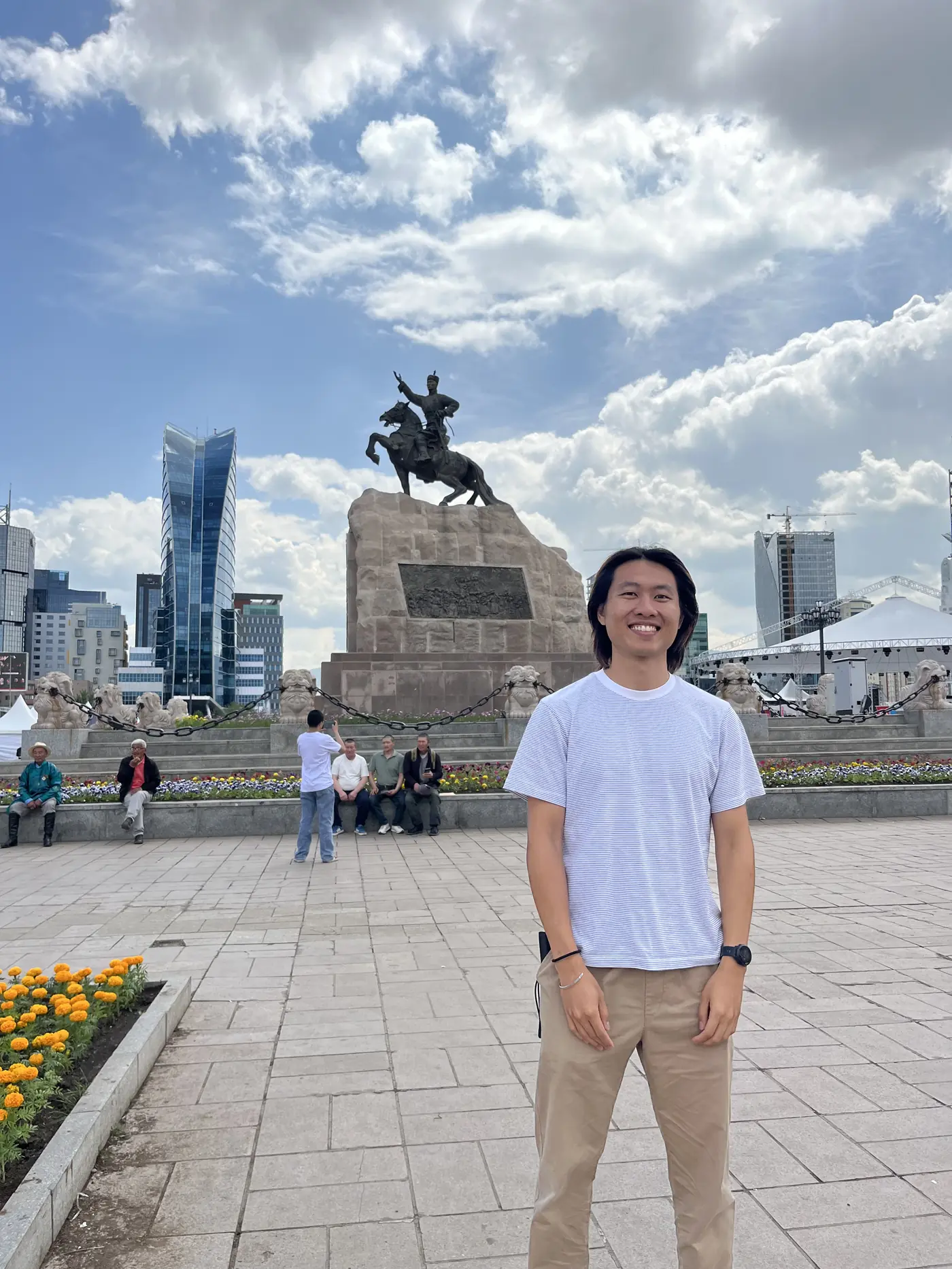 Shin smiling at Sukhbaatar Square, Ulaanbaatar, with the bronze equestrian statue and city skyline behind him
