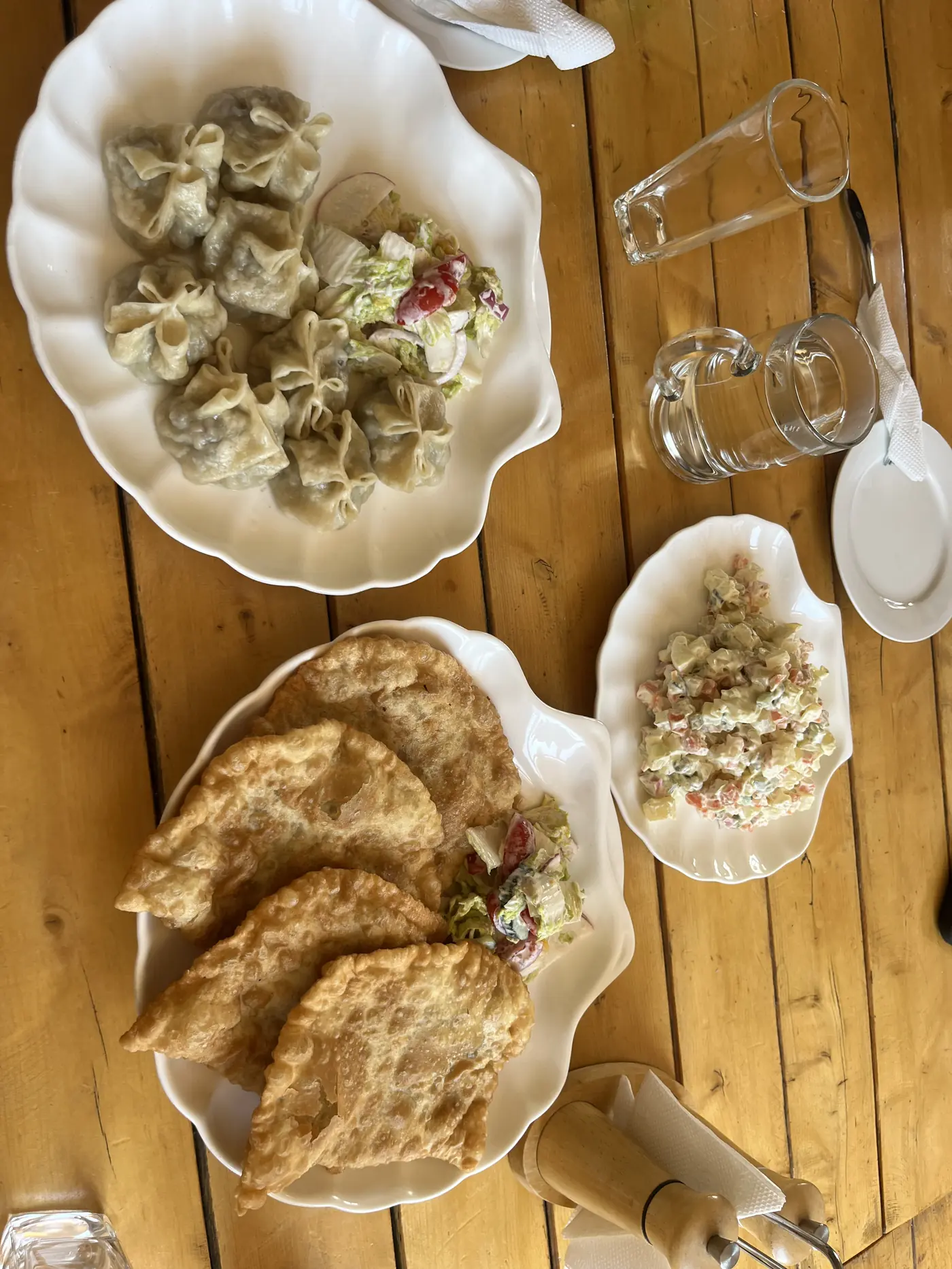 Traditional Mongolian meal overhead shot — buuz dumplings, khuushuur fried pastry, and salad on wooden table in Ulaanbaatar restaurant