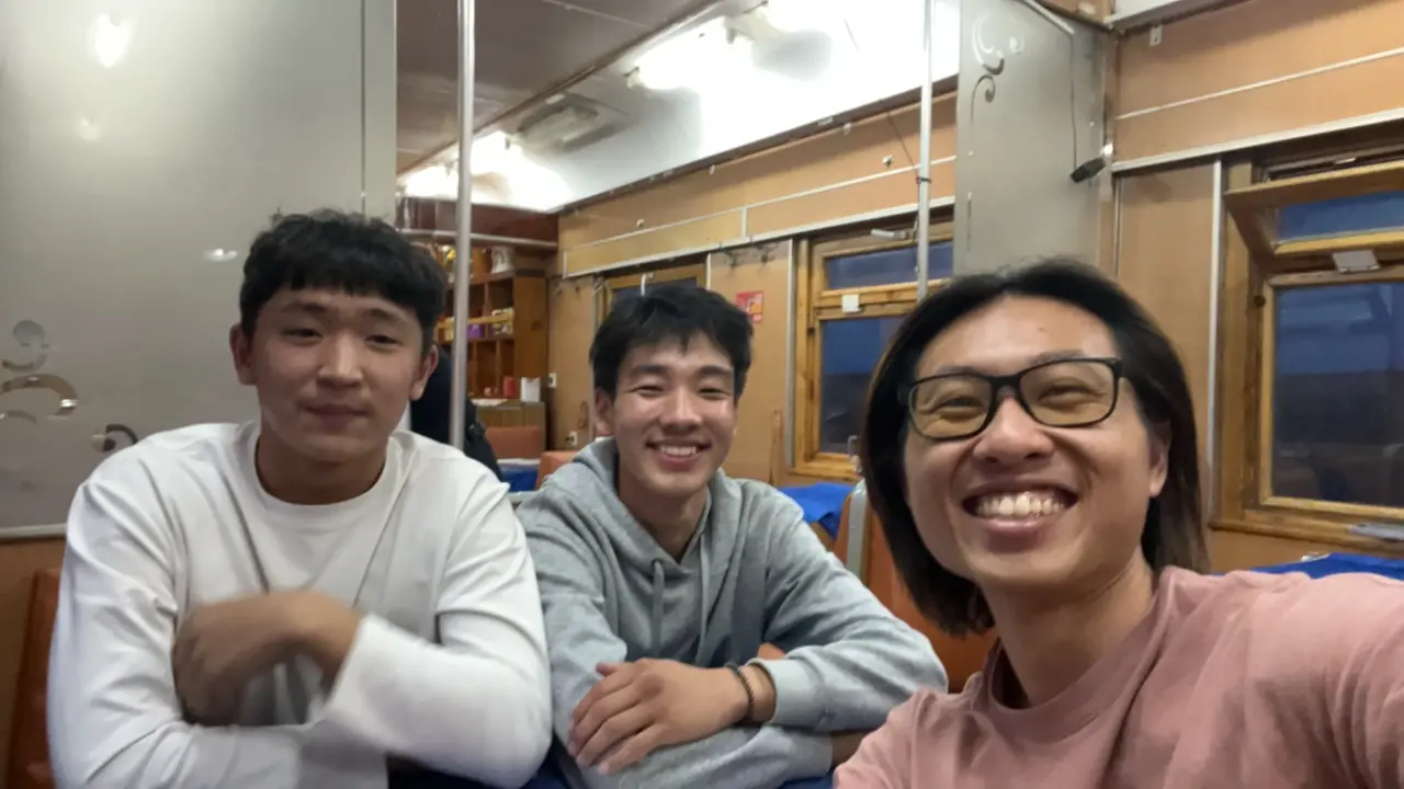 Three travellers laughing together in Trans-Mongolian Railway dining car at night crossing Mongolia