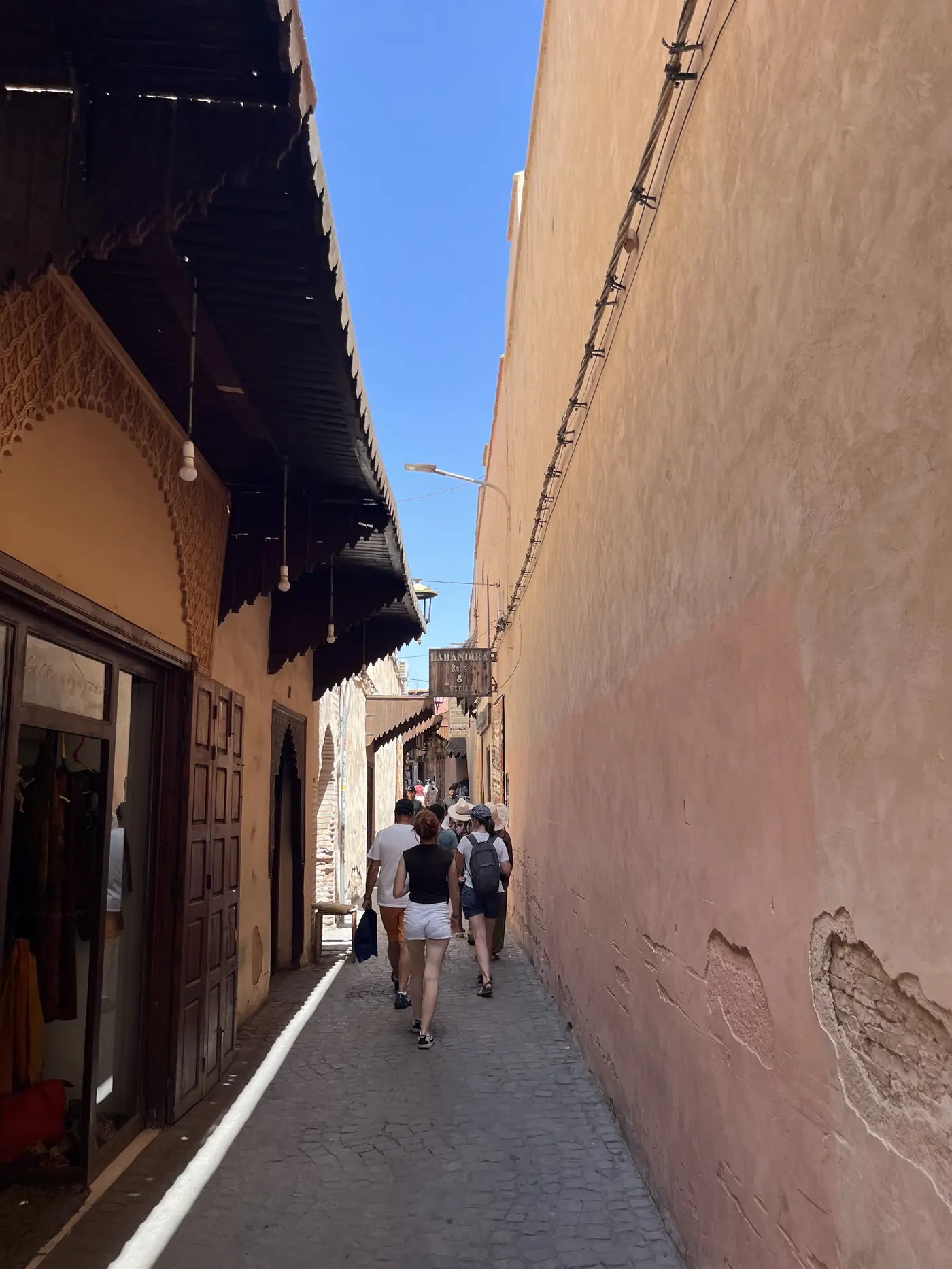 A narrow covered alley in the Marrakech medina with warm ochre walls and shoppers walking past storefronts