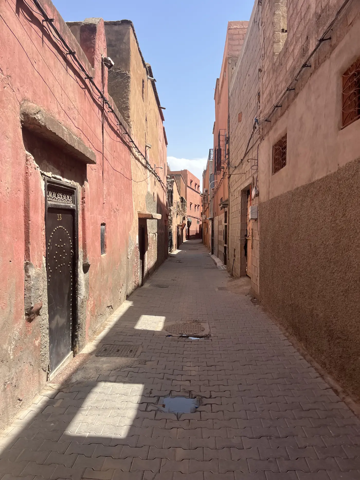 An empty medina alley in Marrakech with weathered pink and terracotta walls and an ornate carved wooden door