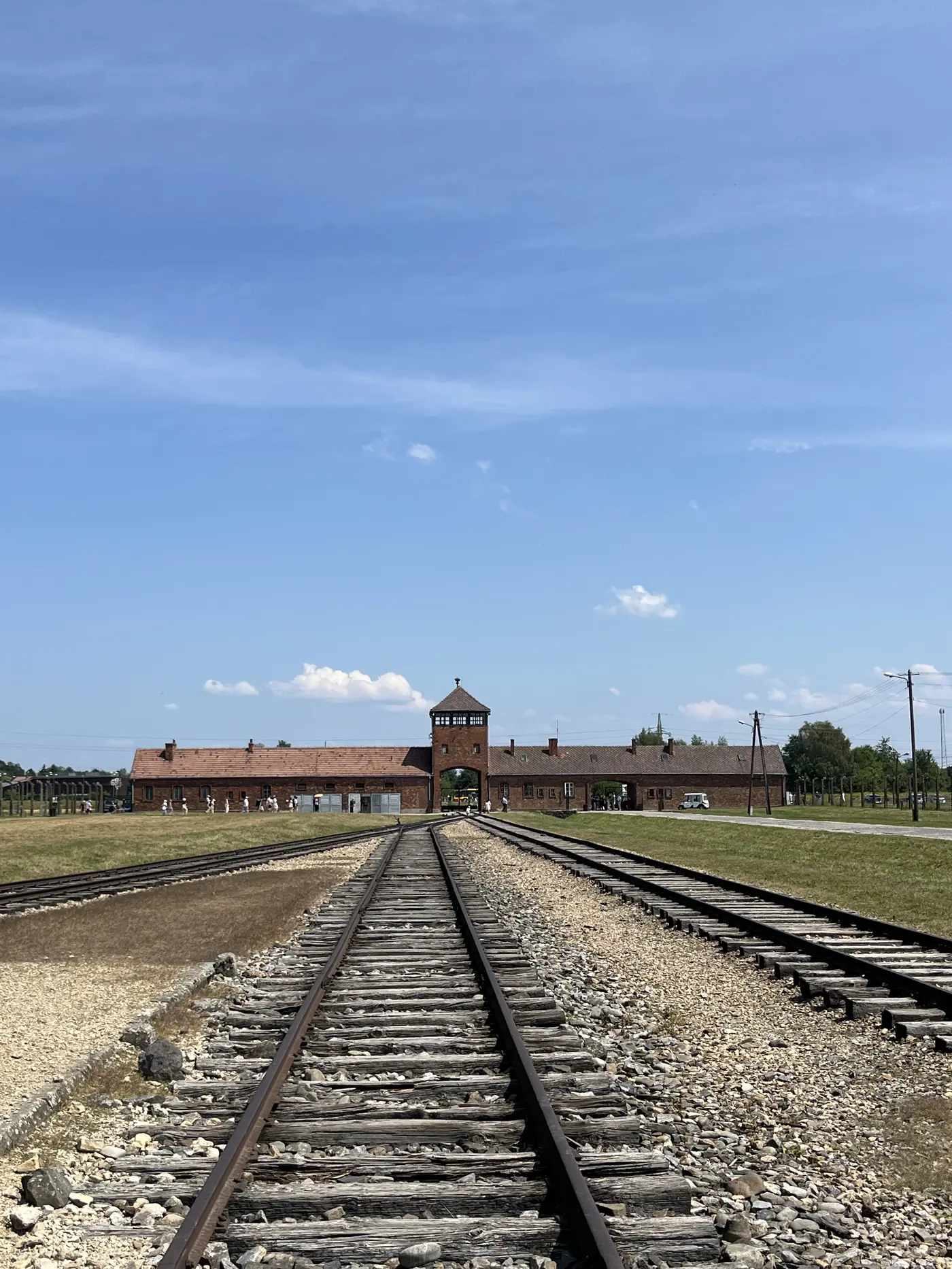 Railway tracks leading to the brick gatehouse of Auschwitz-Birkenau, the so-called Gate of Death, under a clear blue sky