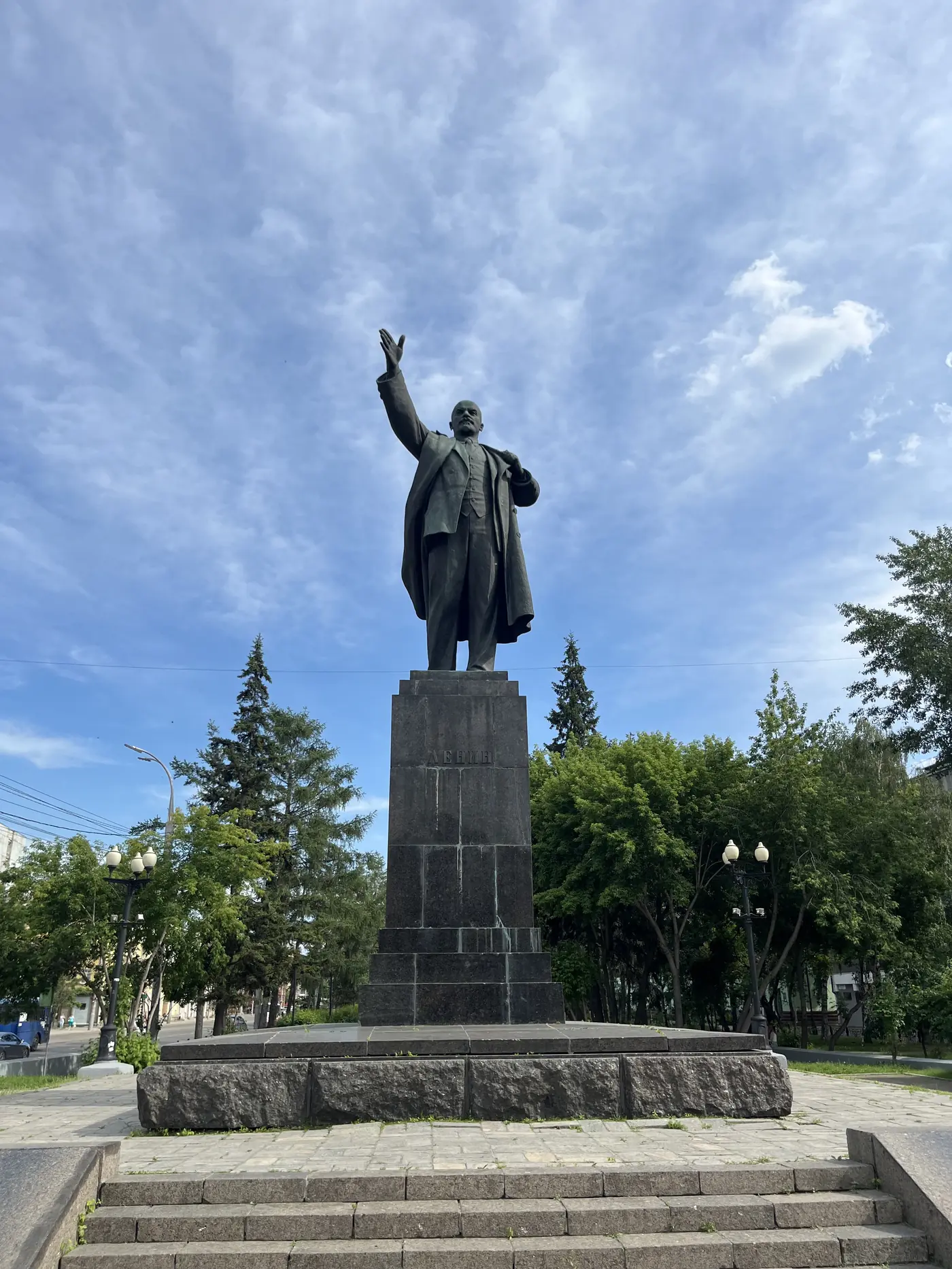 Lenin statue in Irkutsk city centre, arm raised, under blue sky with trees, Soviet-era monument in Siberia Russia