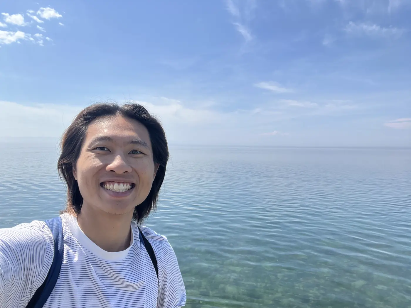 Shin smiling with crystal-clear turquoise Lake Baikal water behind him at Listvyanka village shore, Siberia Russia