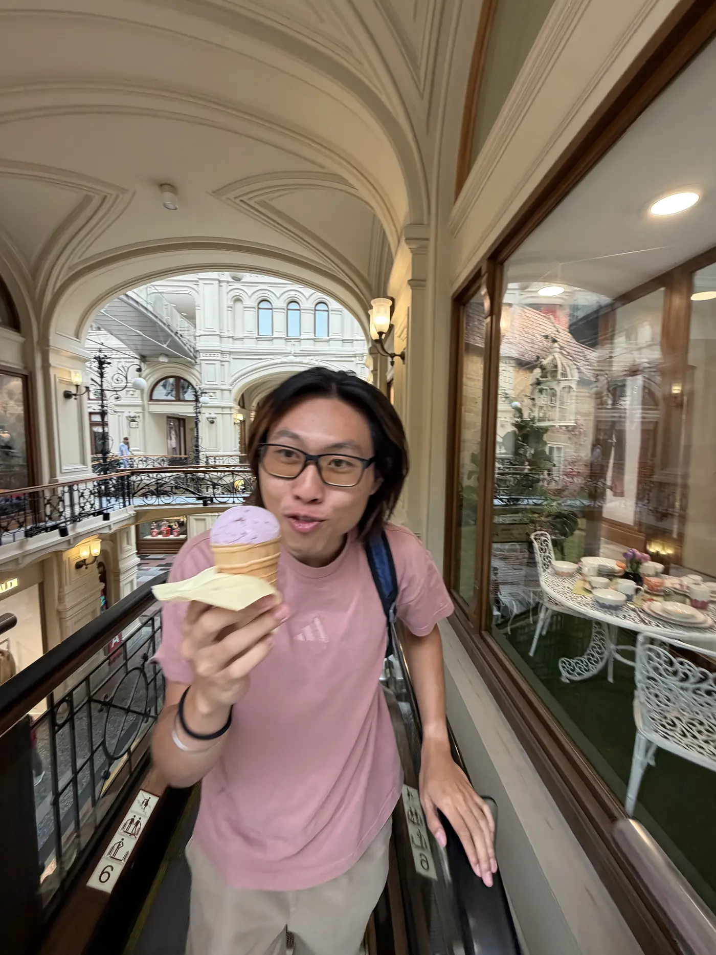 Shin holding a pink scoop of ice cream in a waffle cone inside GUM department store's arcaded glass-roofed gallery, Moscow