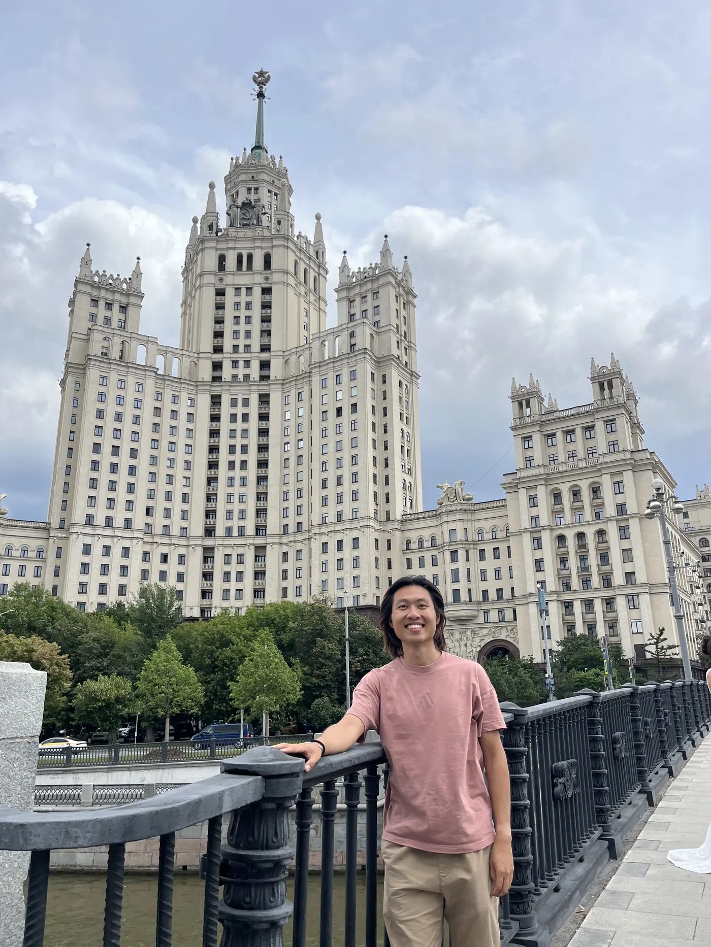 Shin smiling in front of Kotelnicheskaya Embankment Building, one of Stalin's Seven Sisters skyscrapers in Moscow, by the river