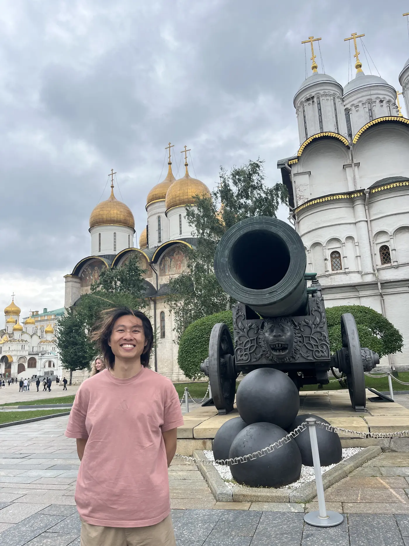 Shin standing beside the Tsar Cannon in the Moscow Kremlin, with the golden domes of the Cathedral of the Dormition behind him