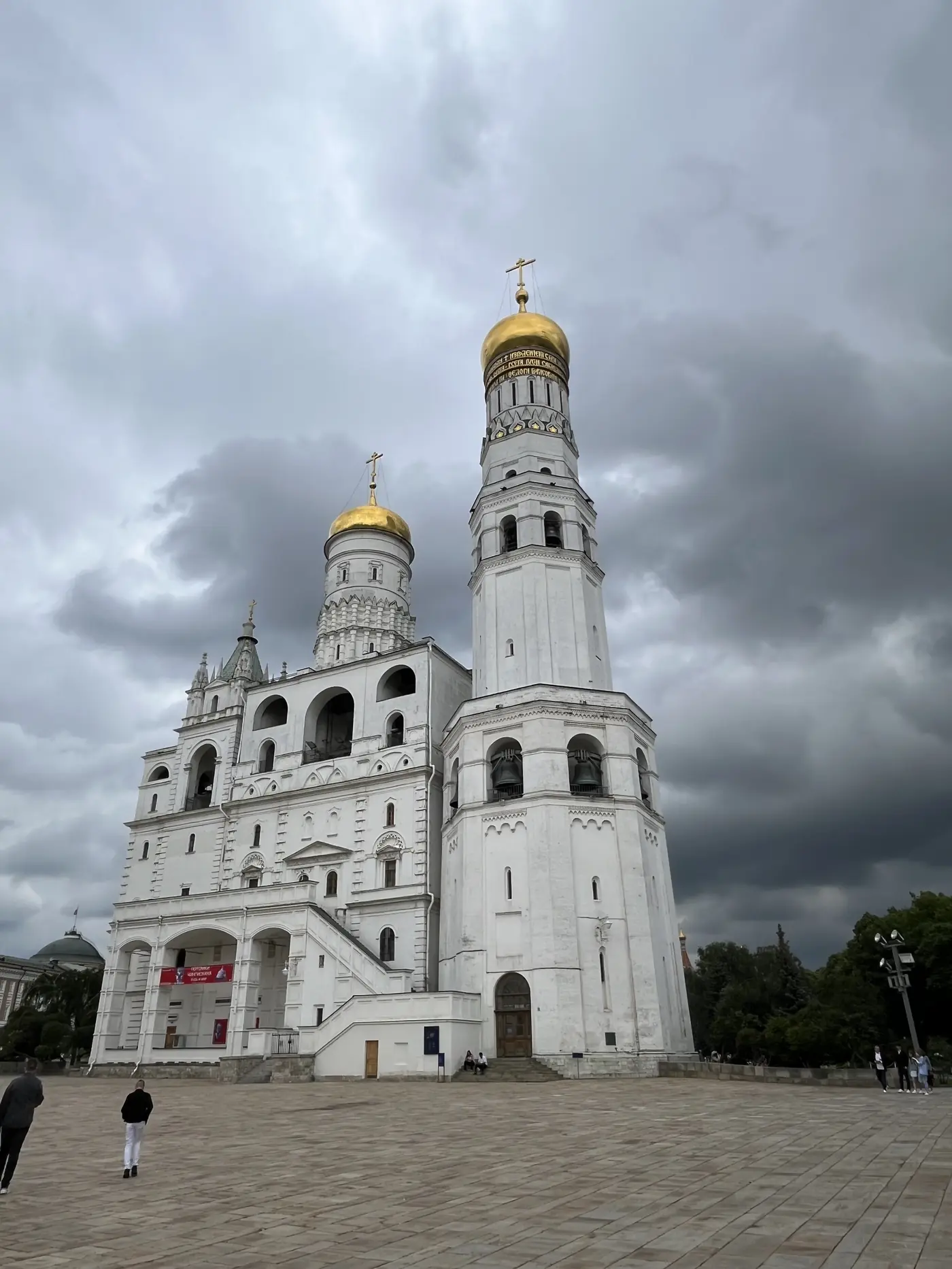 Ivan the Great Bell Tower rising above the Moscow Kremlin under a stormy grey sky, golden domes catching the light