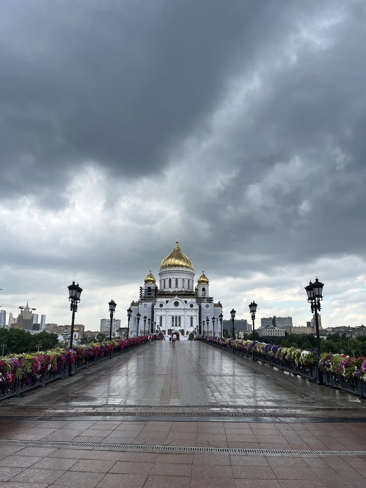 Cathedral of Christ the Saviour viewed from the Patriarshiy pedestrian bridge approach, Moscow, golden dome under stormy sky, flower-lined path