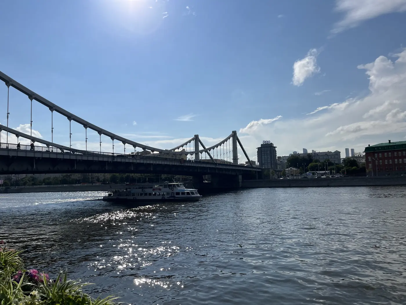Krymsky Bridge suspension bridge over the Moscow River on a sunny day, river cruise boat passing underneath, city skyline behind