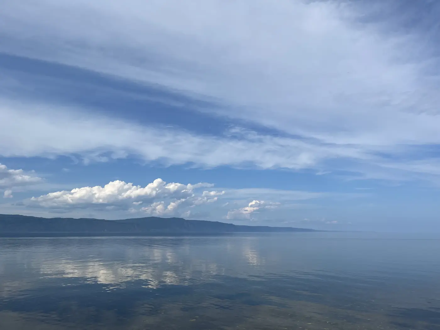 Lake Baikal panorama from Slyudyanka shore, mirror-calm water reflecting the sky, distant mountain ridge, Siberia Russia