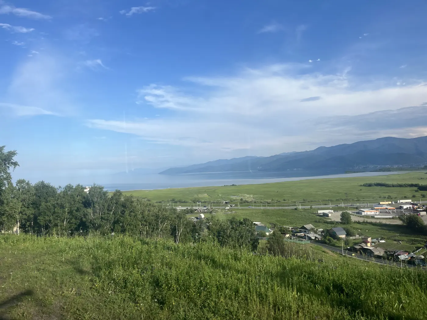 Hillside panoramic view of Slyudyanka town with Lake Baikal stretching into the distance, green meadows and Siberian mountains