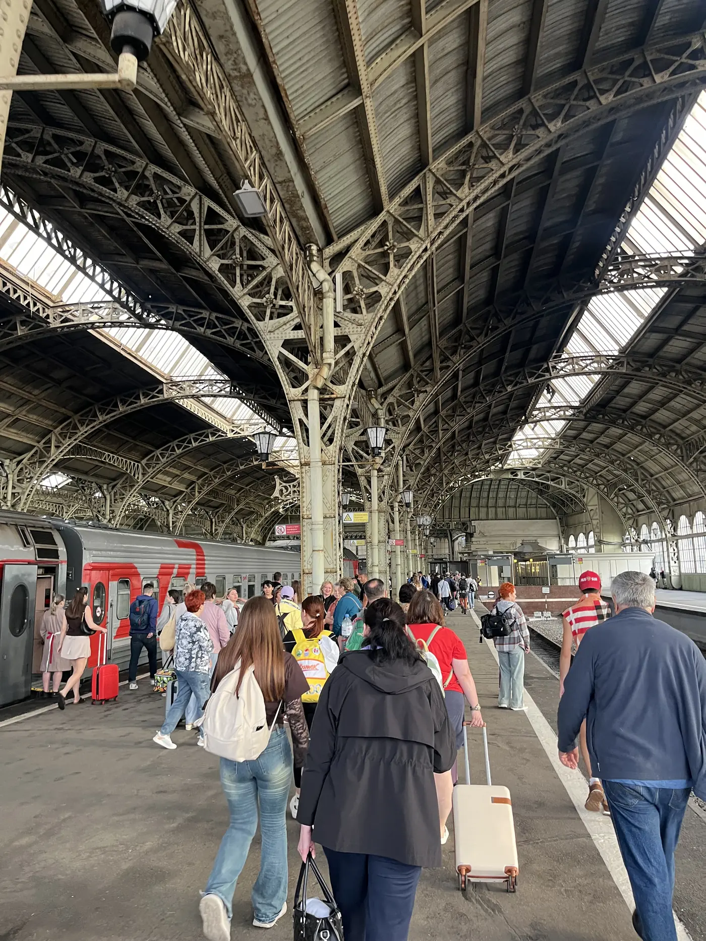 Interior of Vitebsky railway station in St. Petersburg with magnificent cast-iron arched roof and passengers boarding a red RZhD train